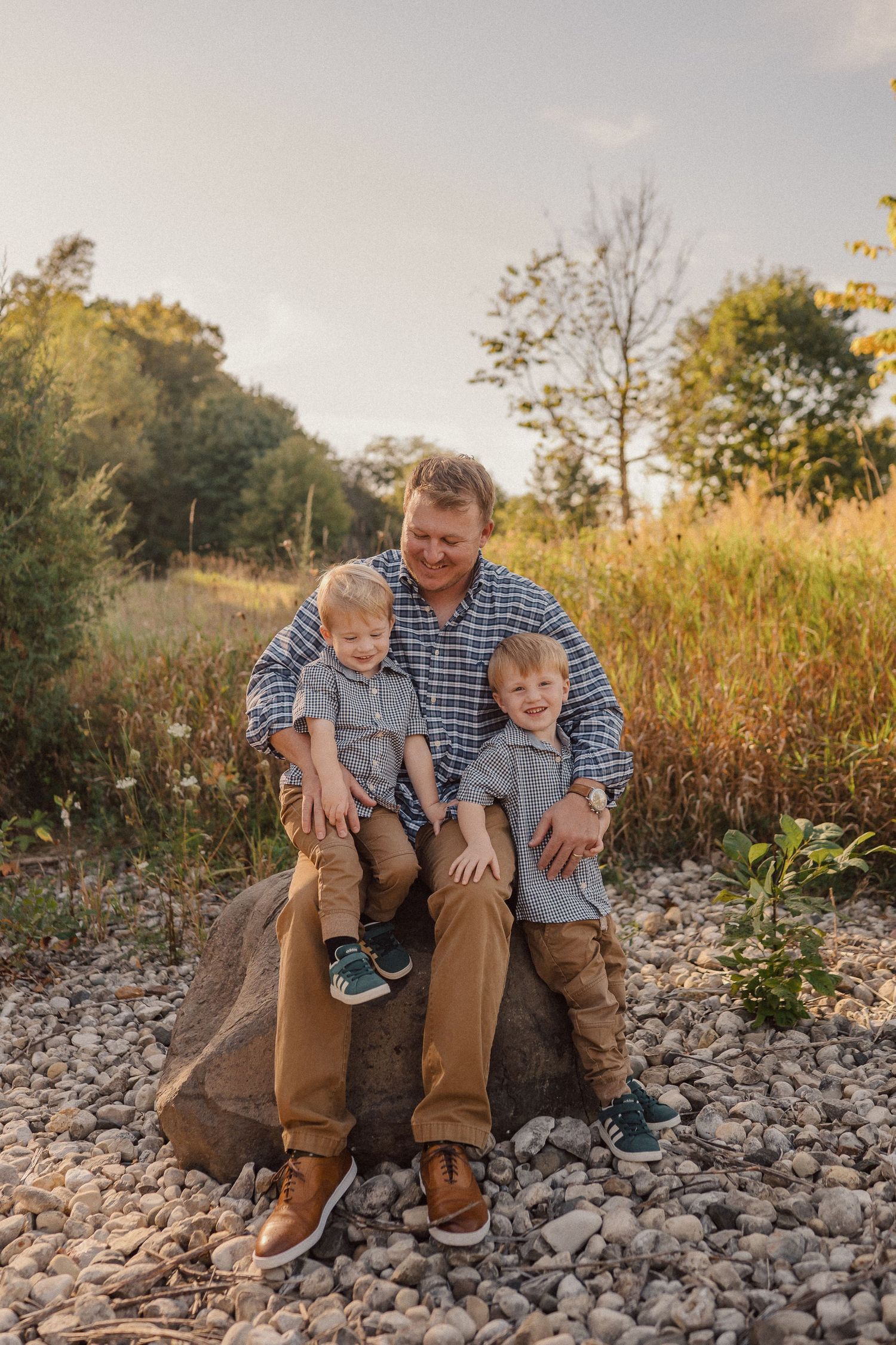 A heartwarming outdoor family portrait taken on rocky terrain with golden grasses in the background.