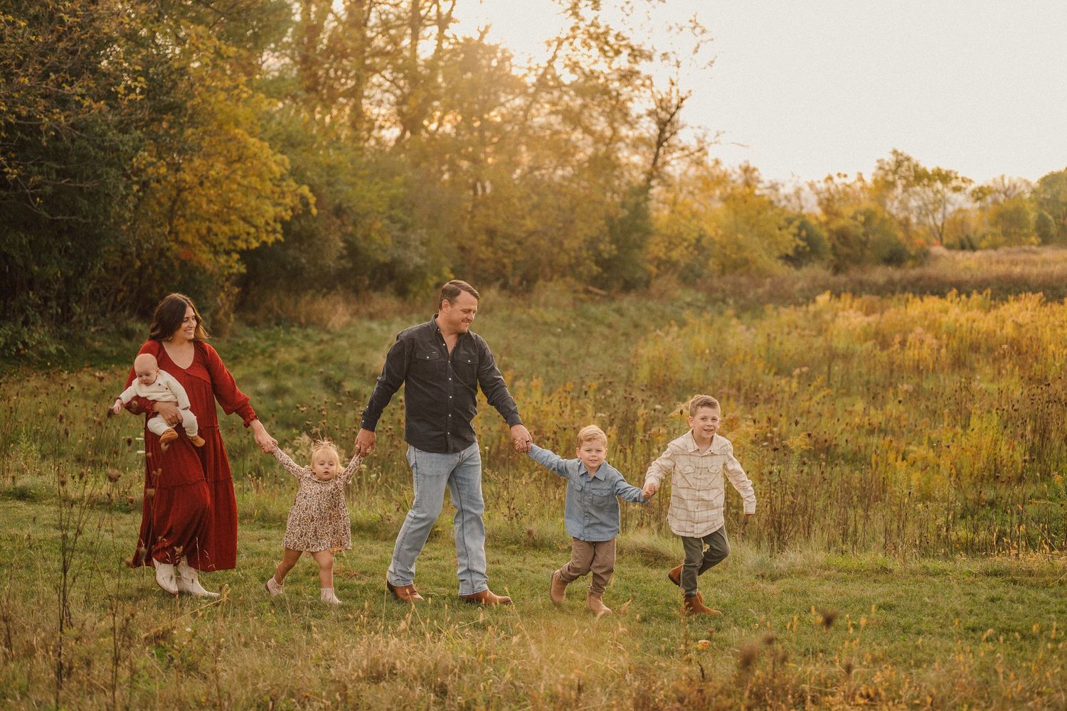 Family walking together hand in hand through golden field at sunset.