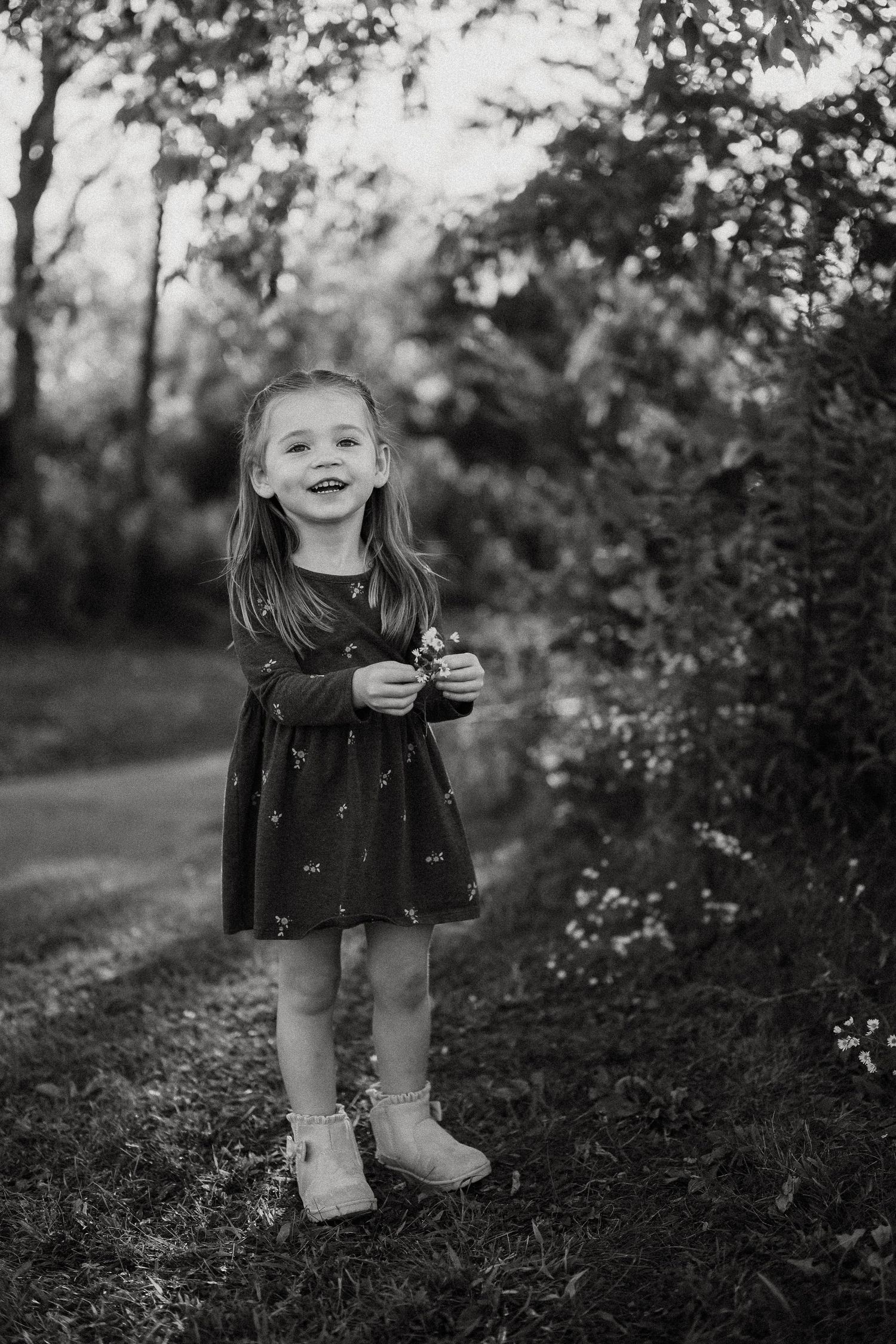 Black and white photo of a child exploring through tall grass and wildflowers at sunset.