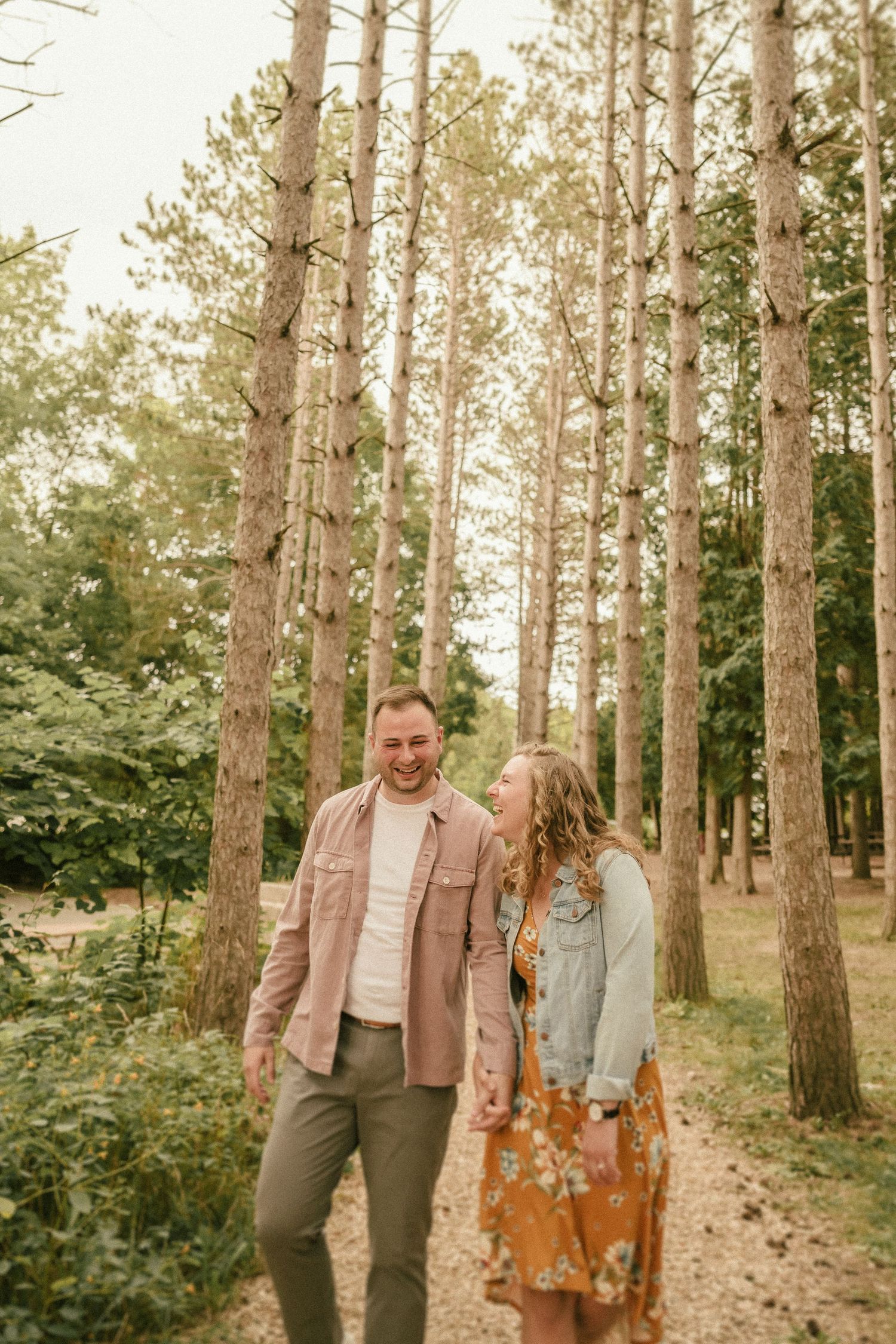 Couple shares a joyful moment while walking through a tall pine forest.