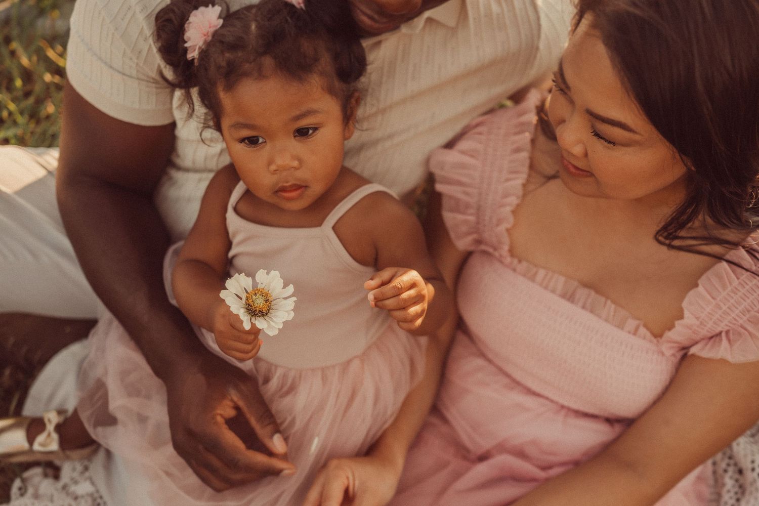 Family shares a tender moment outdoors while holding a small white flower.