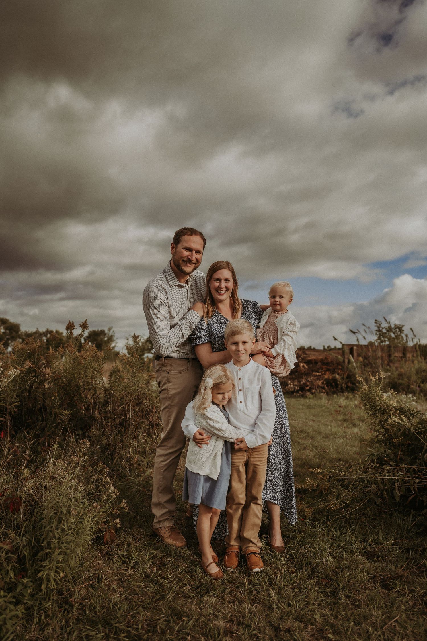 Natural family portrait on a hilltop with dramatic clouds and rustic scenery.