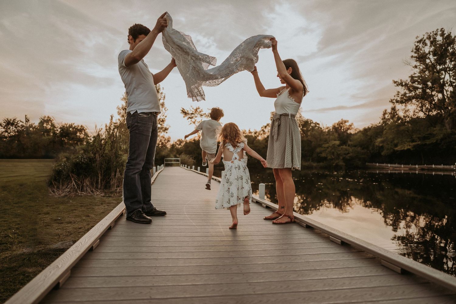 A family plays together on a wooden boardwalk during sunset.