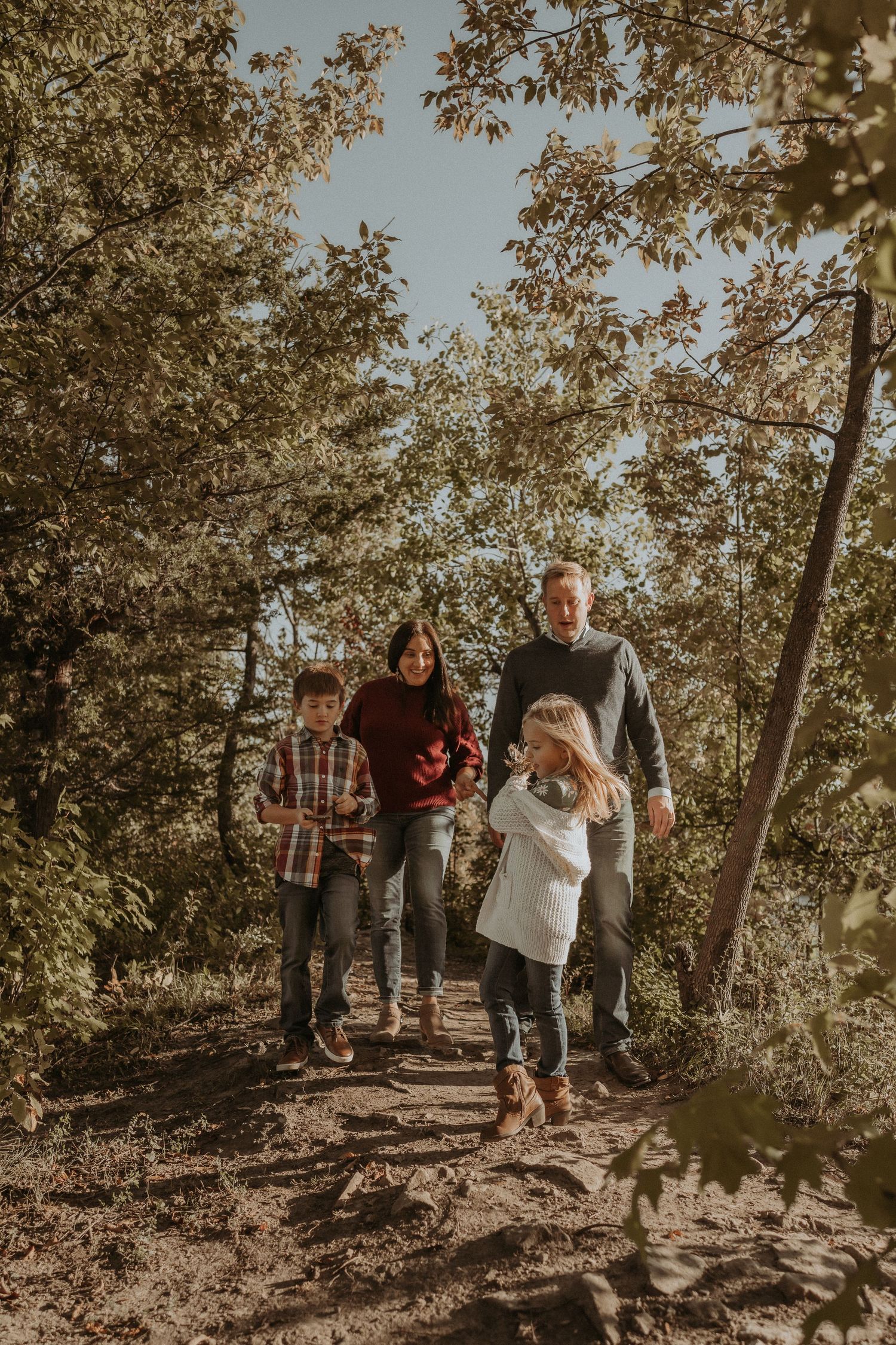 A family walks together on a tree-lined trail during a warm autumn day.