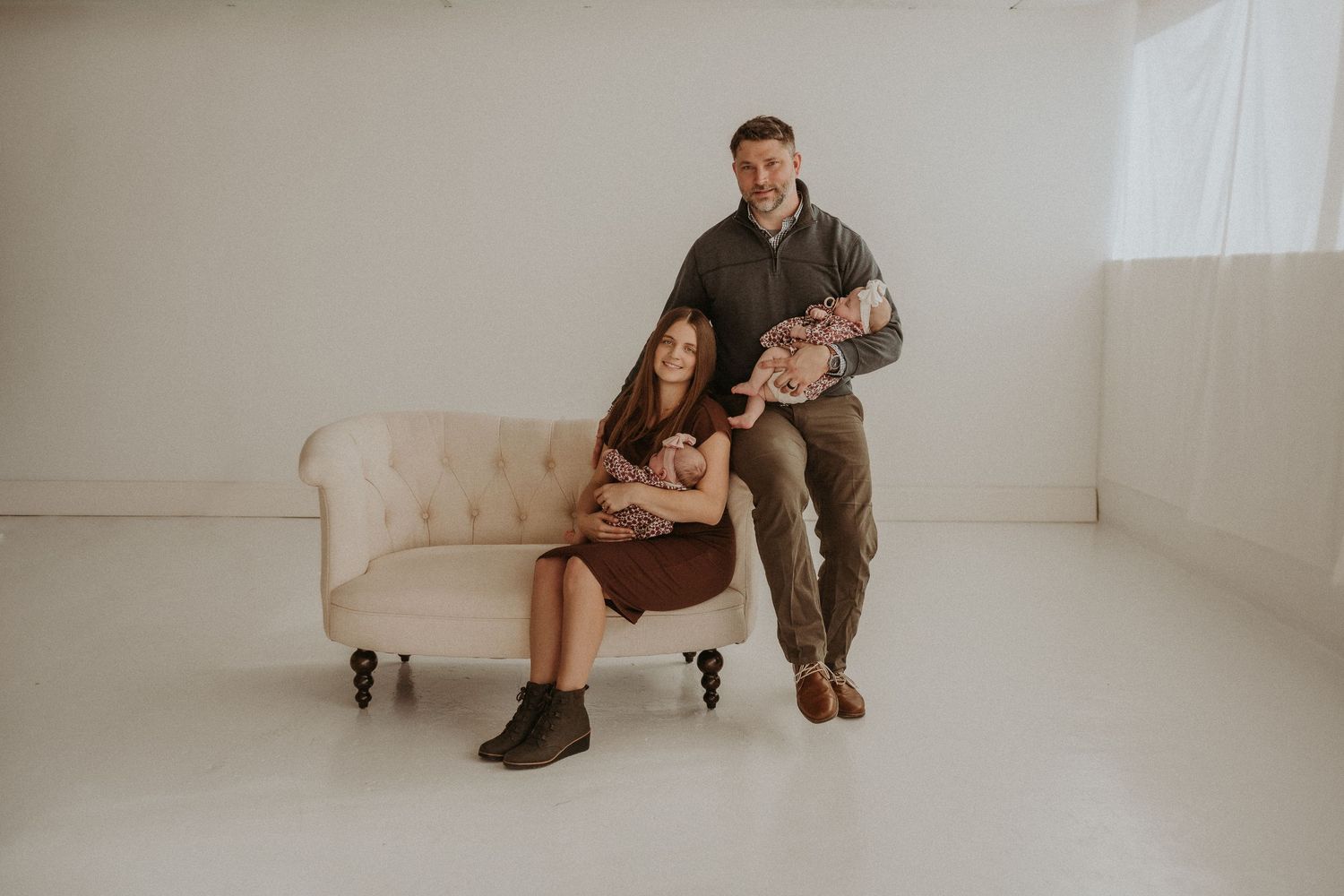 Family portrait in minimalist white studio with people sitting on vintage brown couch.