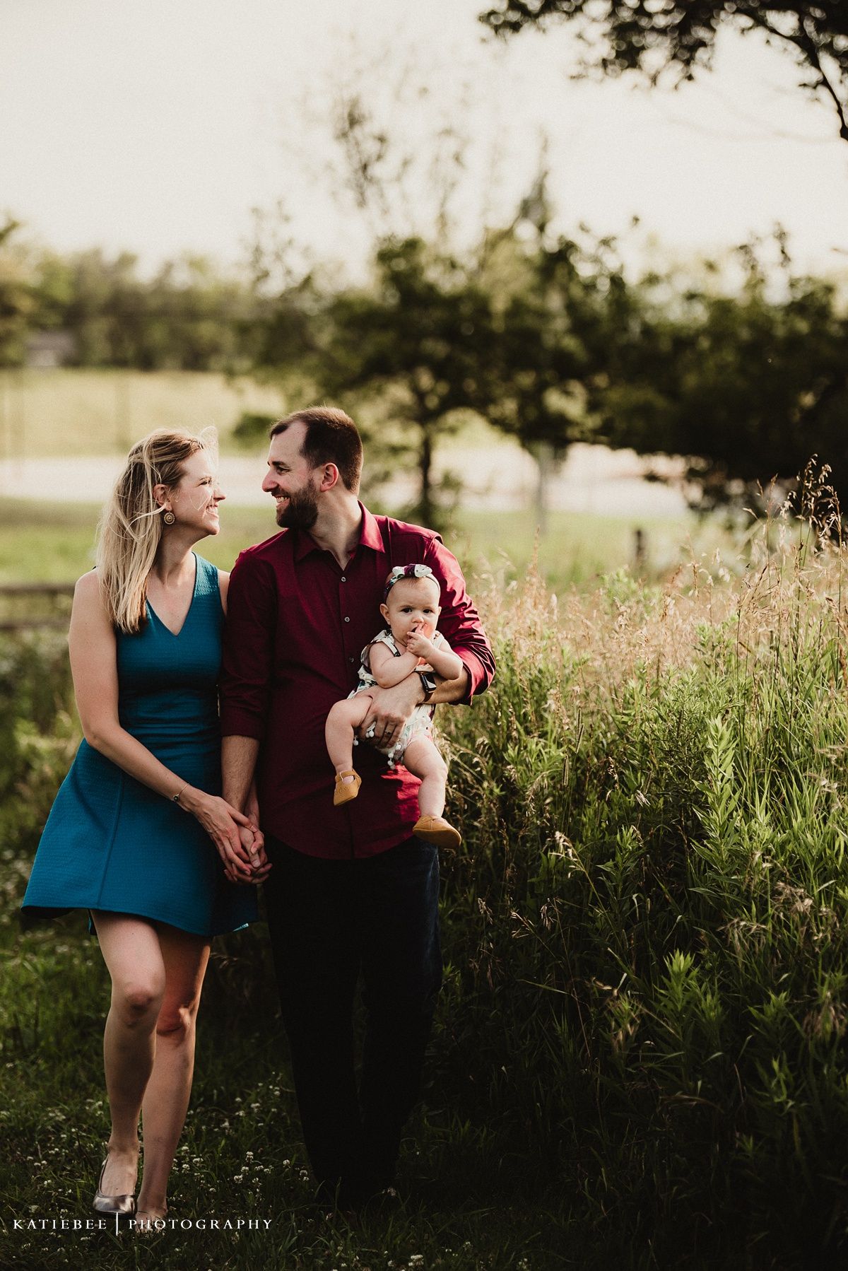 Family shares intimate moment together in sunset-lit field with tall grass.