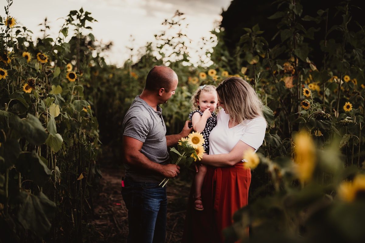 Family sharing joyful moment together among tall sunflowers at sunset.