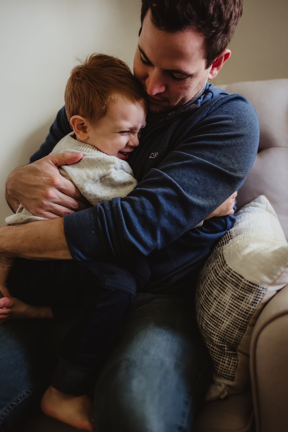 Parent holding infant in white sweater against soft natural window light.