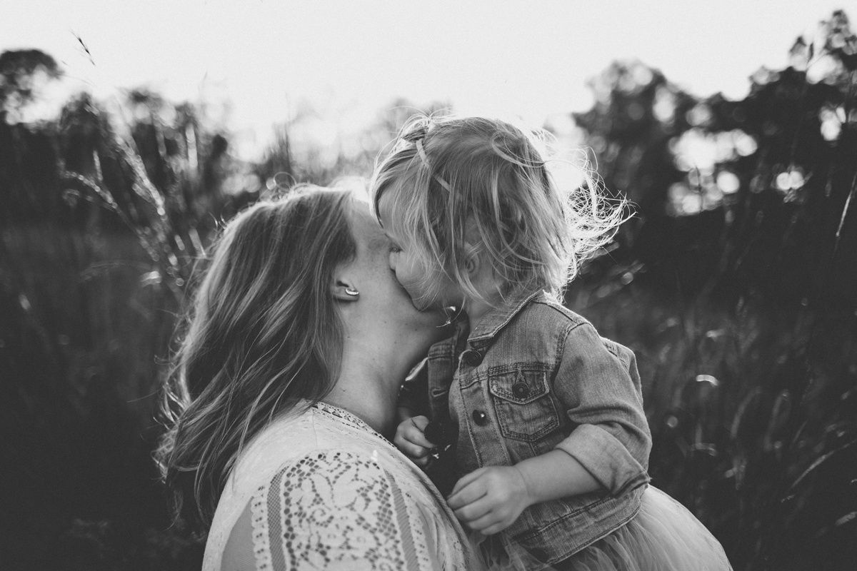 A tender black and white portrait showing an intimate moment between two figures in a sunlit outdoor setting.