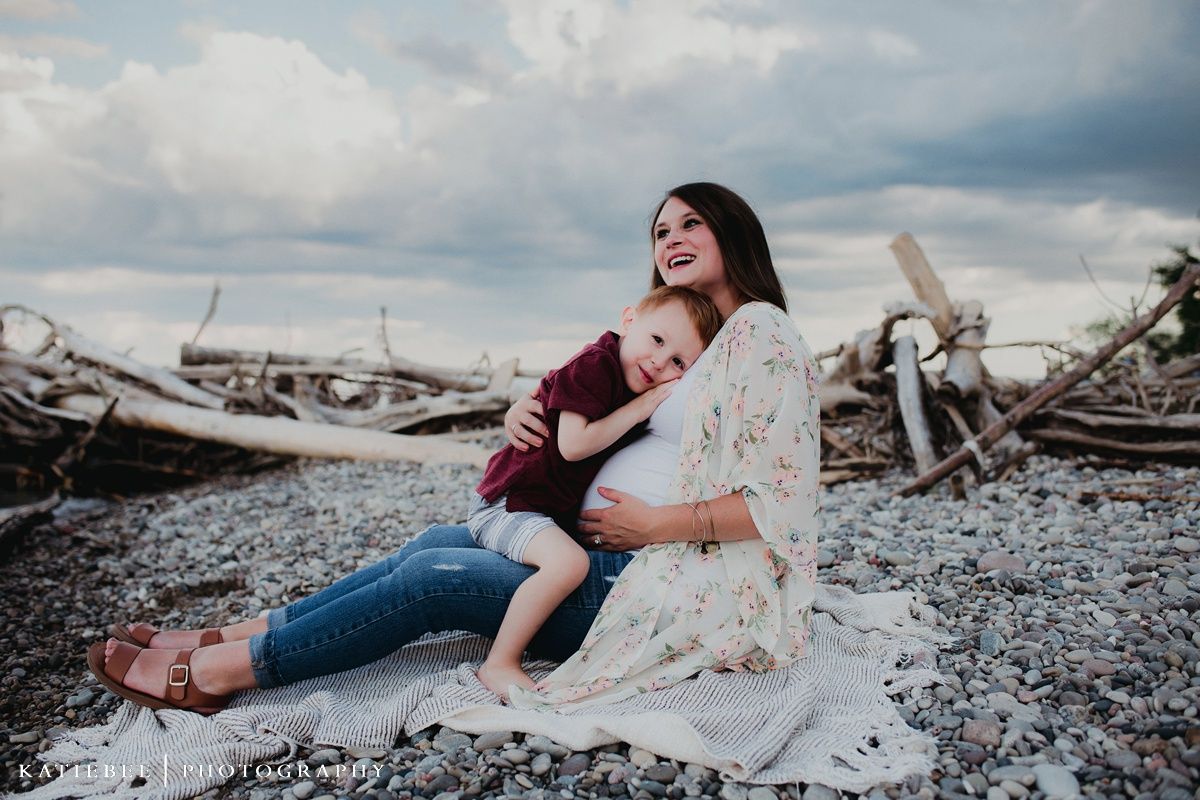 A tender moment captured on a beach with driftwood and cloudy skies in the background.