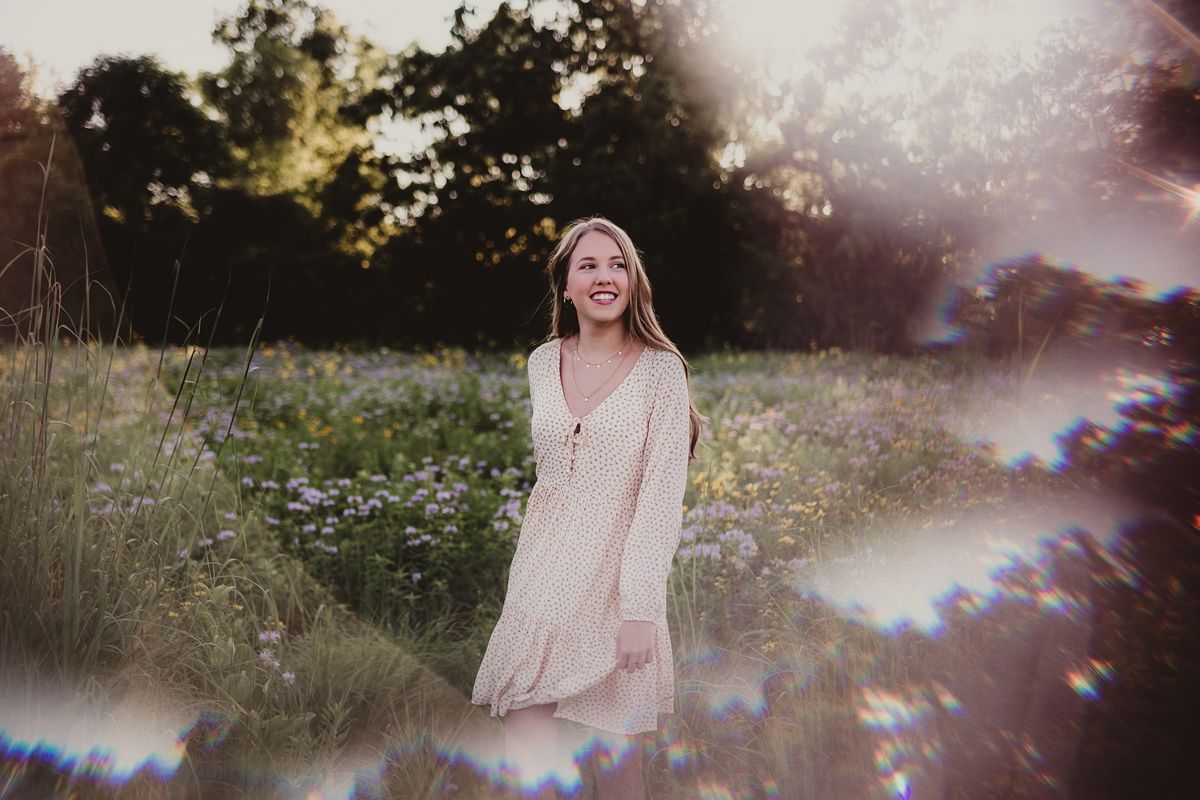 Dreamy portrait with lens flare in a summer meadow at golden hour.