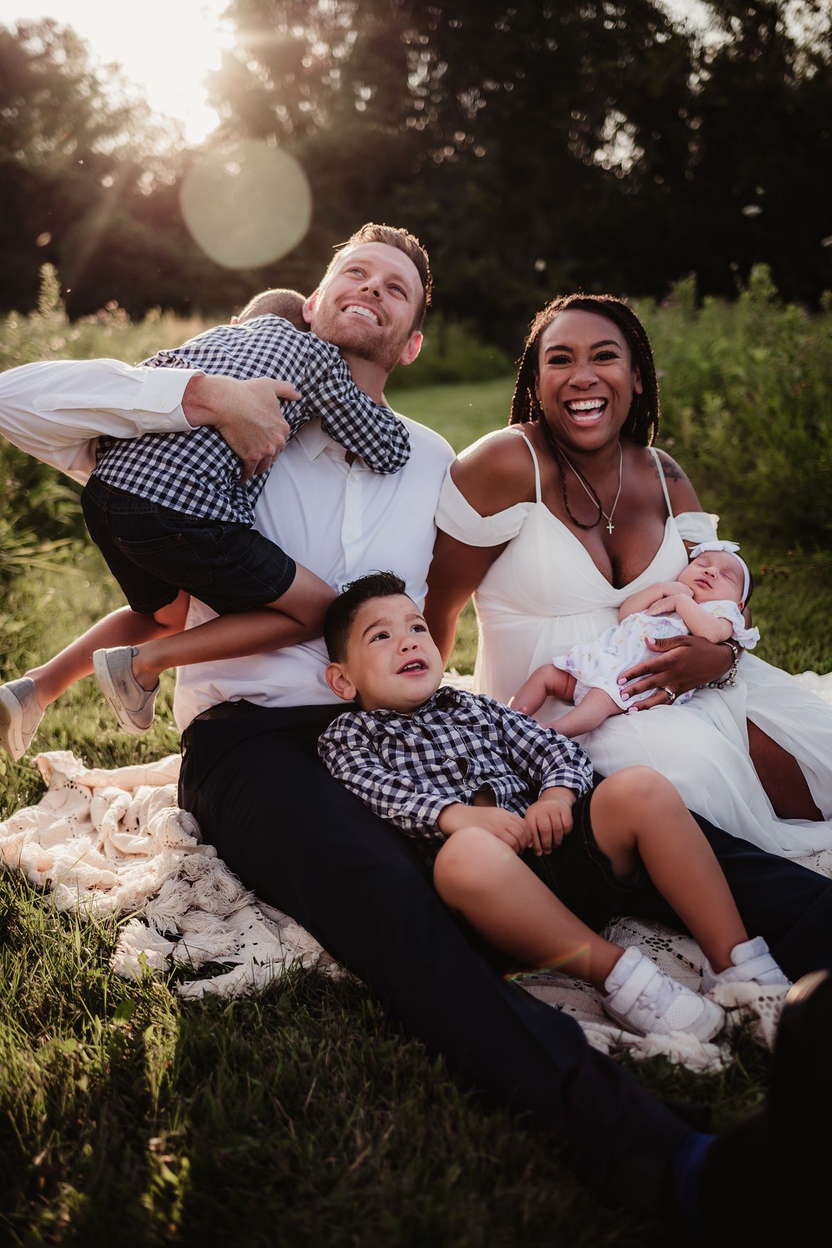 Family relaxing on blanket outdoors during sunset photo session.