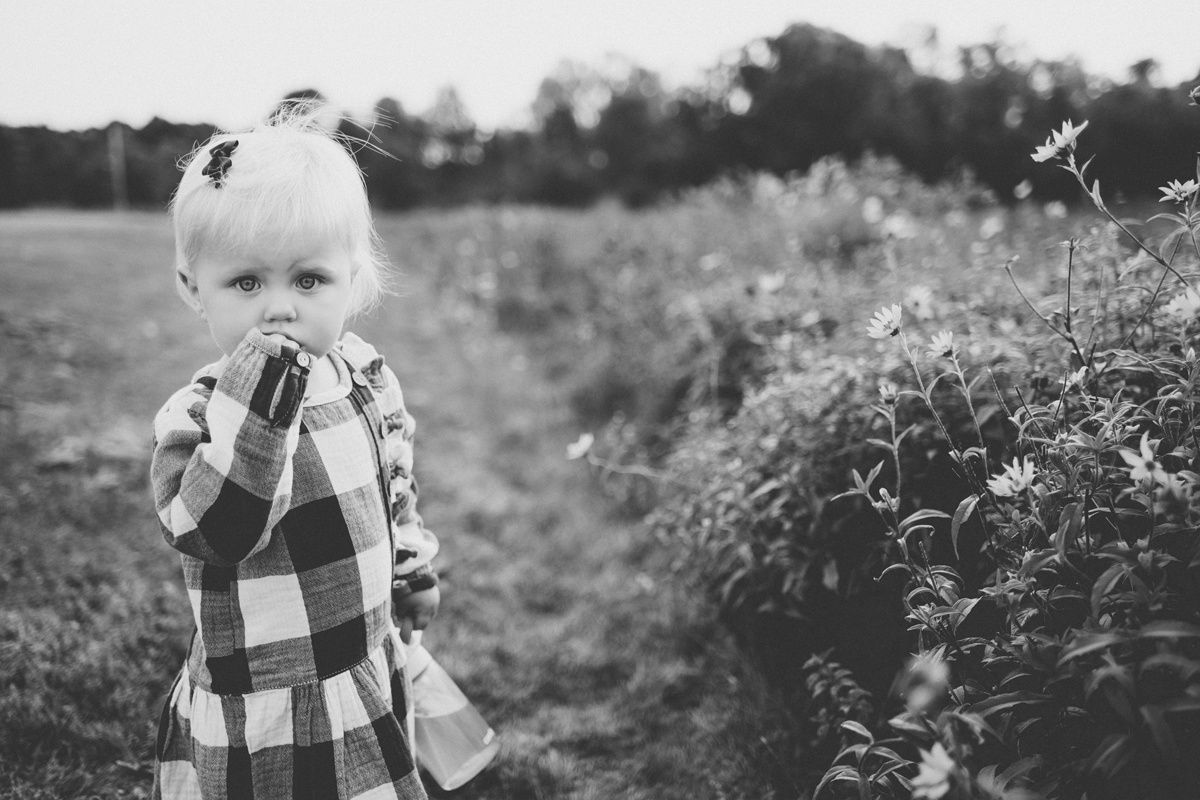 Black and white portrait of small child in plaid dress among wildflowers.