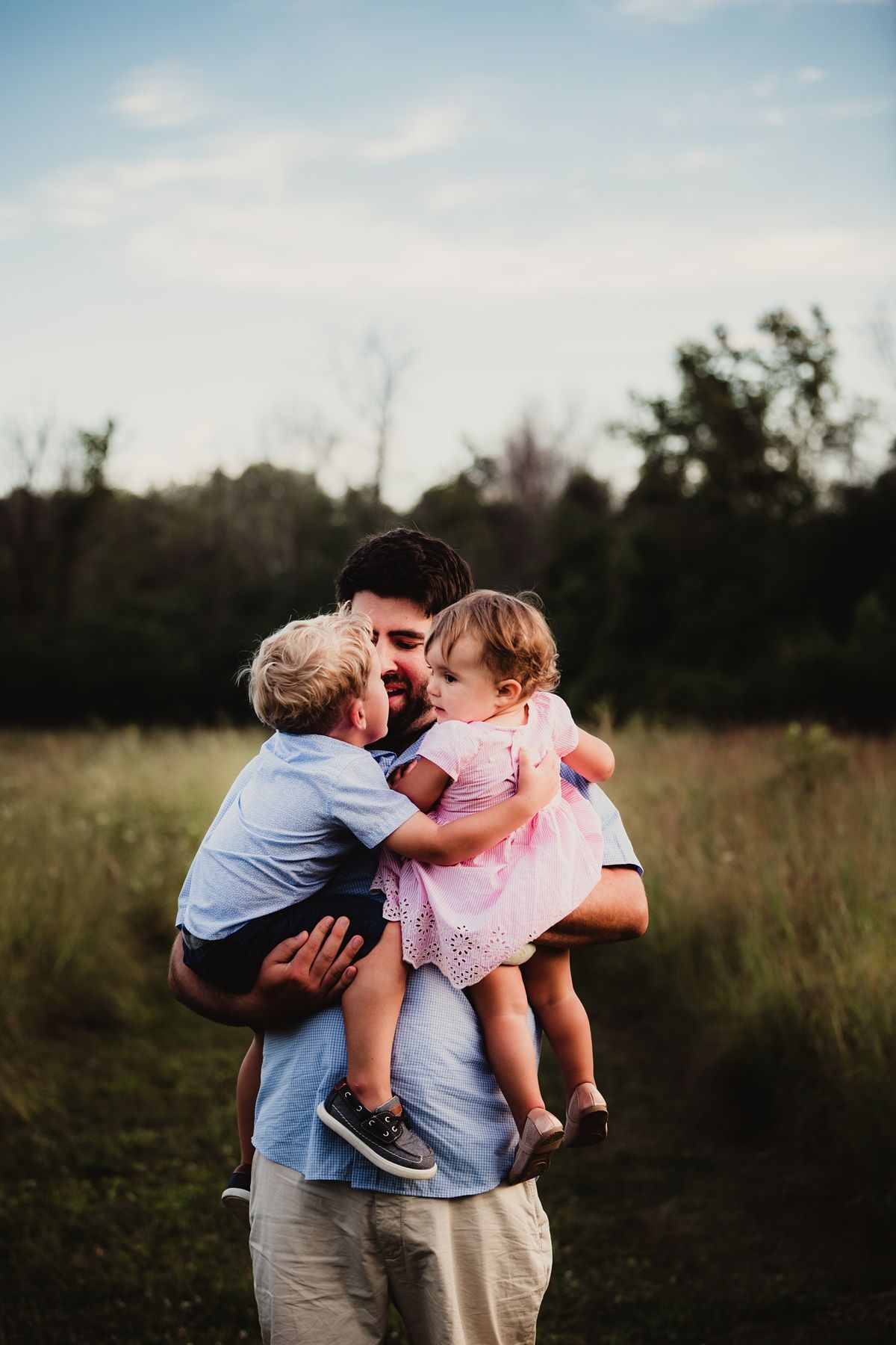 Tender family moment captured at sunset in a grassy field during golden hour.