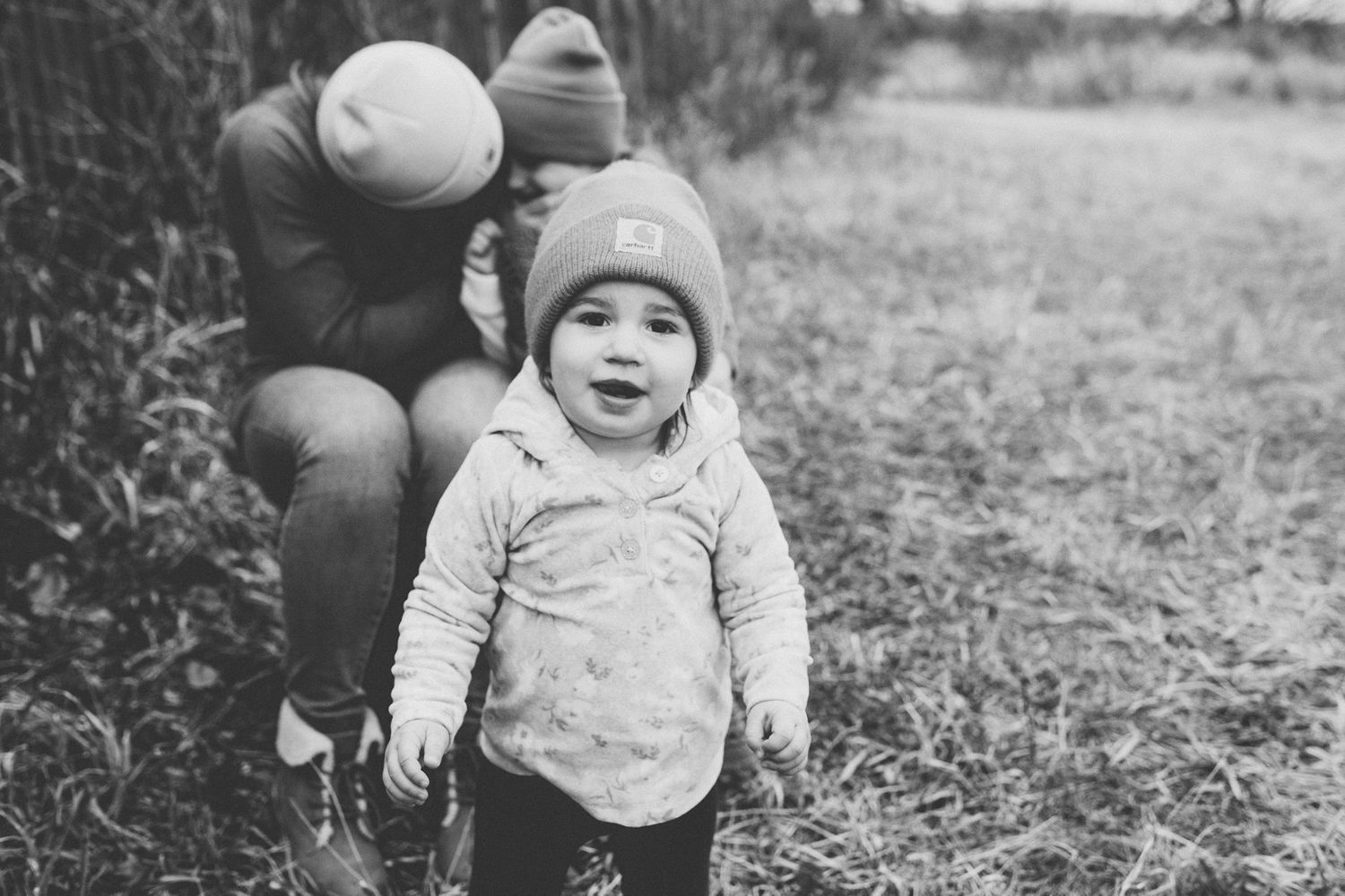 A black and white photo of a small child in winter clothing standing on a path outdoors.