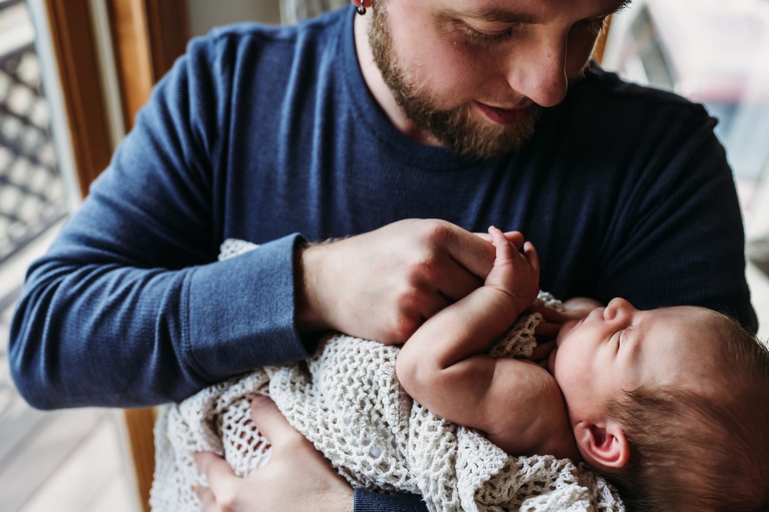 A tender moment between a parent in a navy sweater cradling a tiny baby wearing a polka dot outfit.