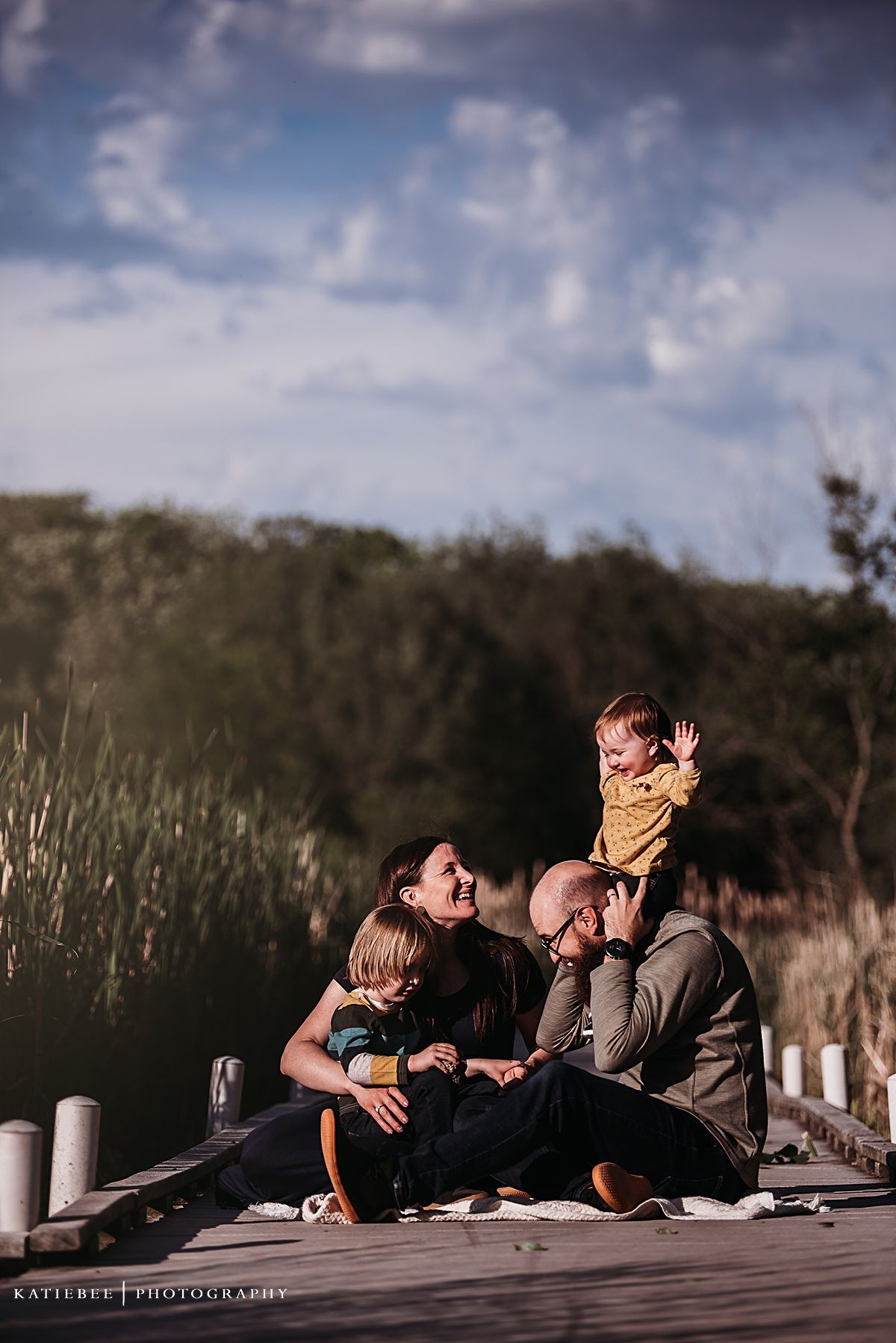 Family enjoys playful moment together on wooden deck during sunset photoshoot.
