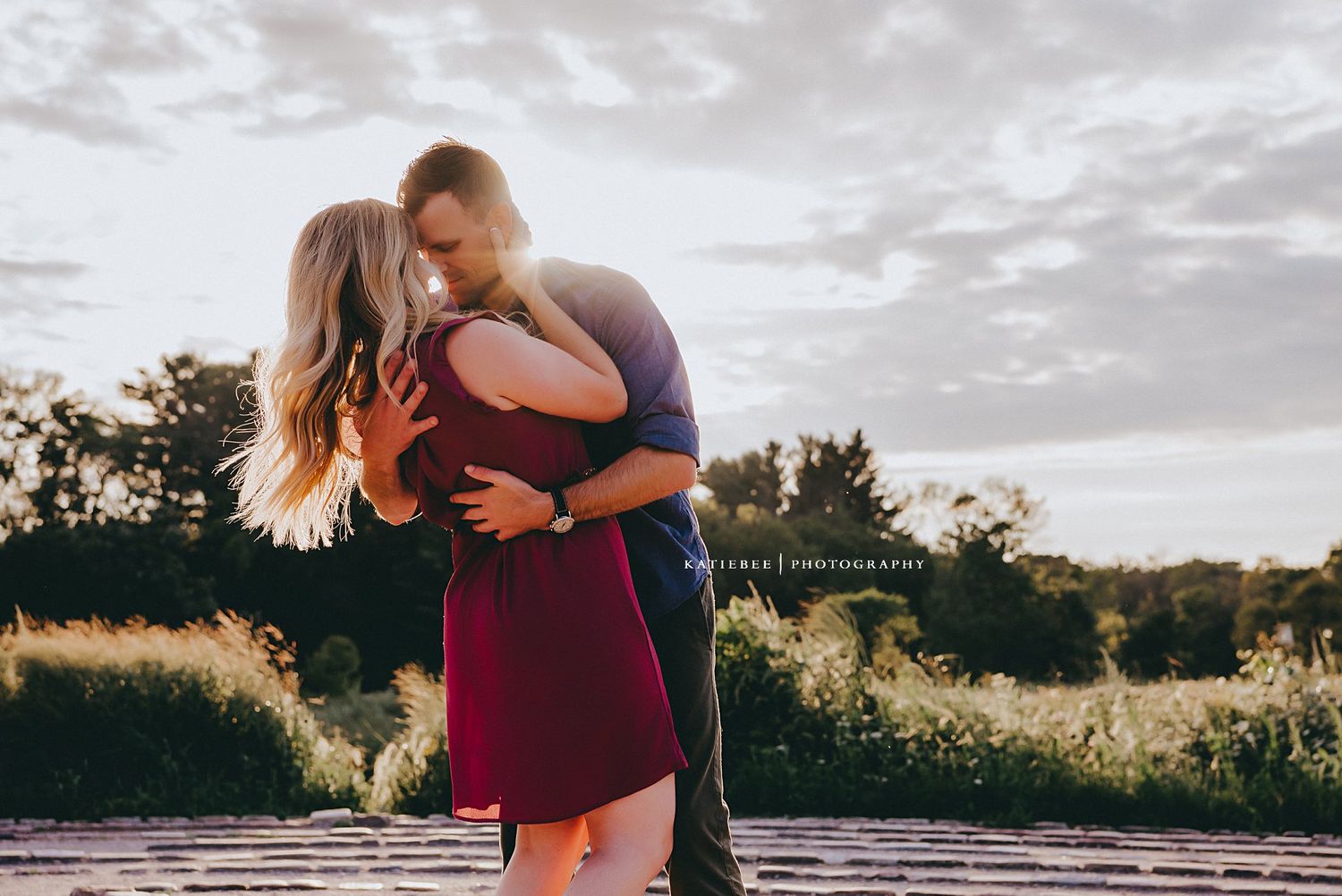 Couple embracing in burgundy dress and blue shirt during sunset in nature.