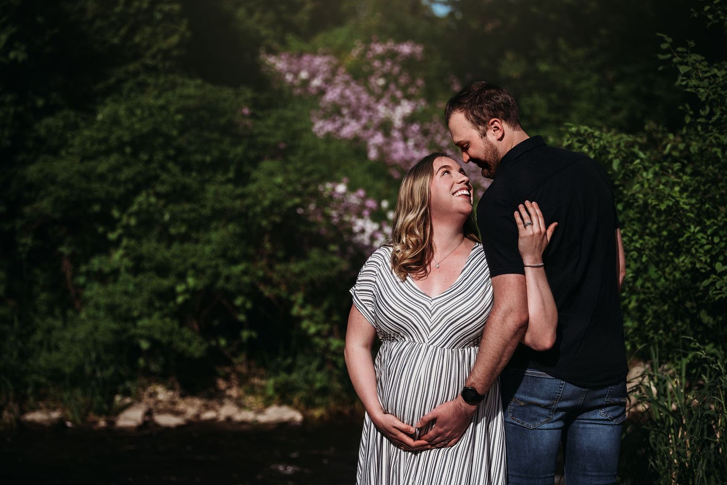 Maternity photo of couple embracing in front of blooming spring trees.