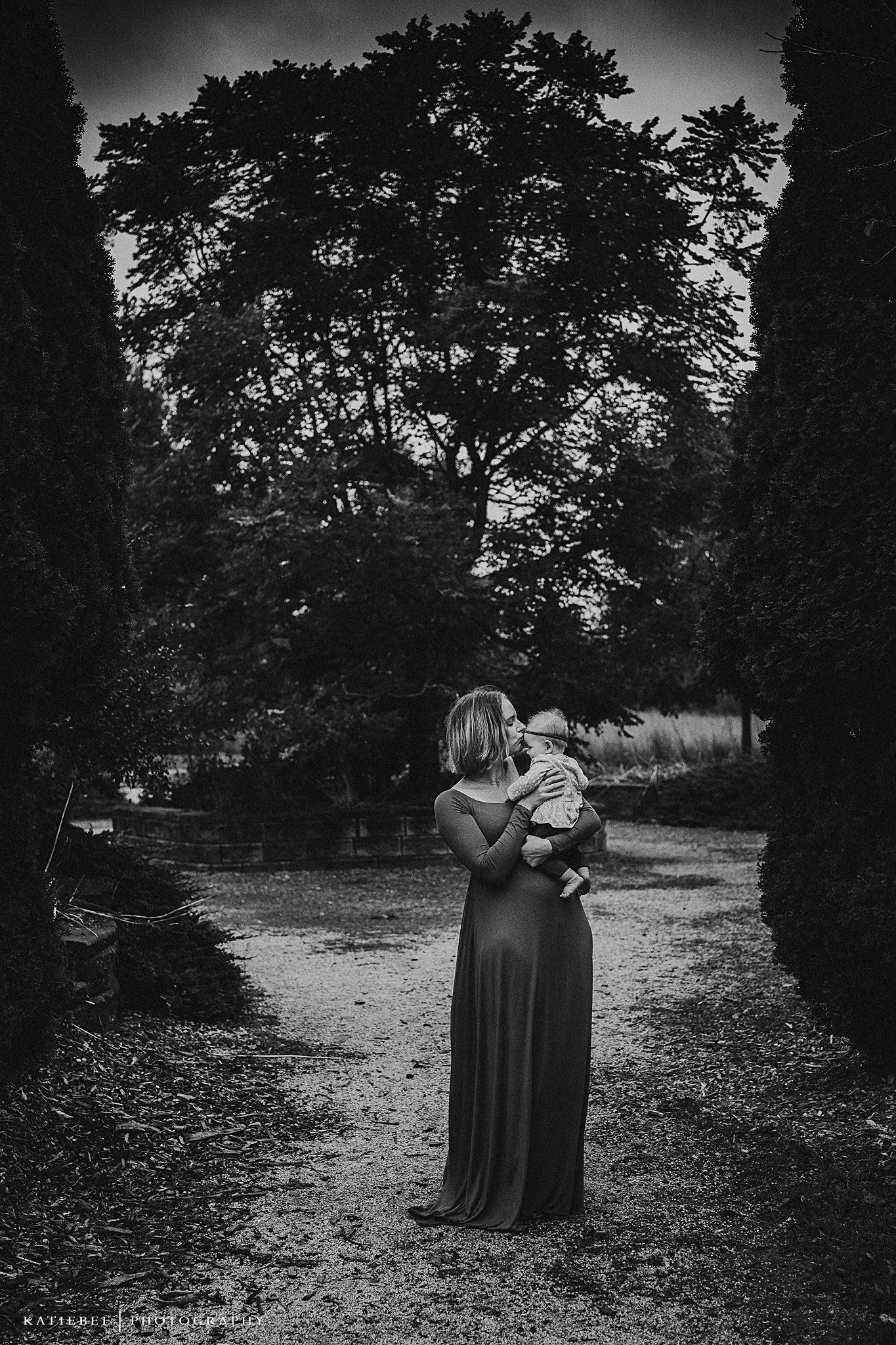 A black and white portrait in a garden path framed by tall evergreen trees.