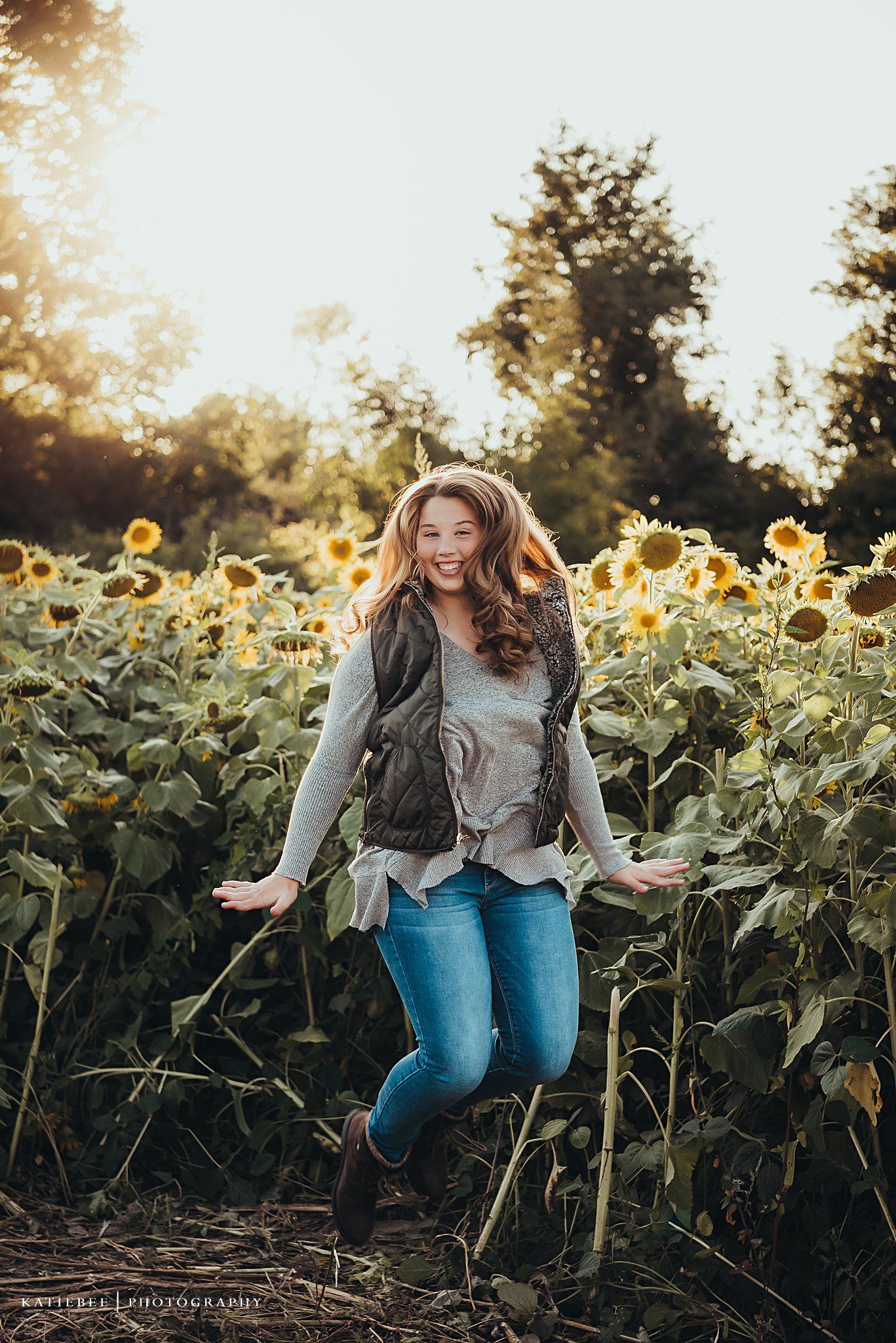 A joyful portrait in a sunflower field at golden hour featuring casual fall outfit with vest and jeans.