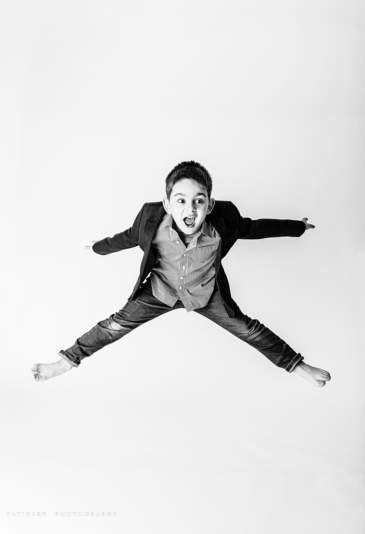 Black and white photo of child jumping with arms and legs spread in star position against white backdrop.