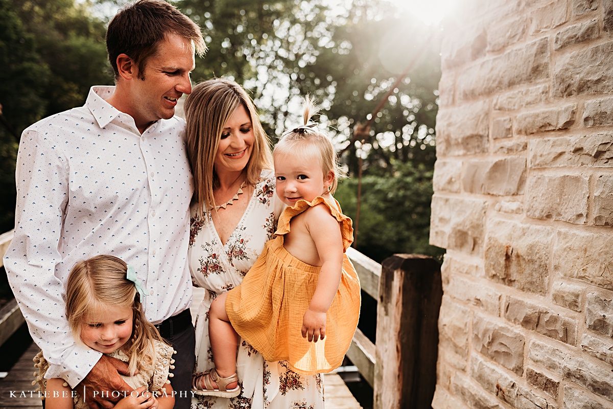 Family of four poses together on rustic bridge with stone architecture.
