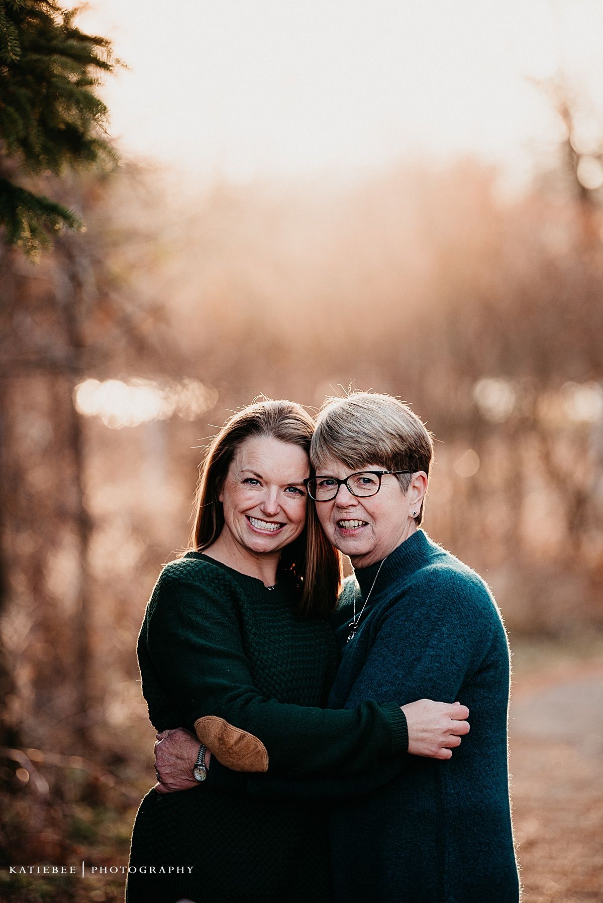 Two people embrace while sharing a genuine laugh together on a wooded path at sunset.