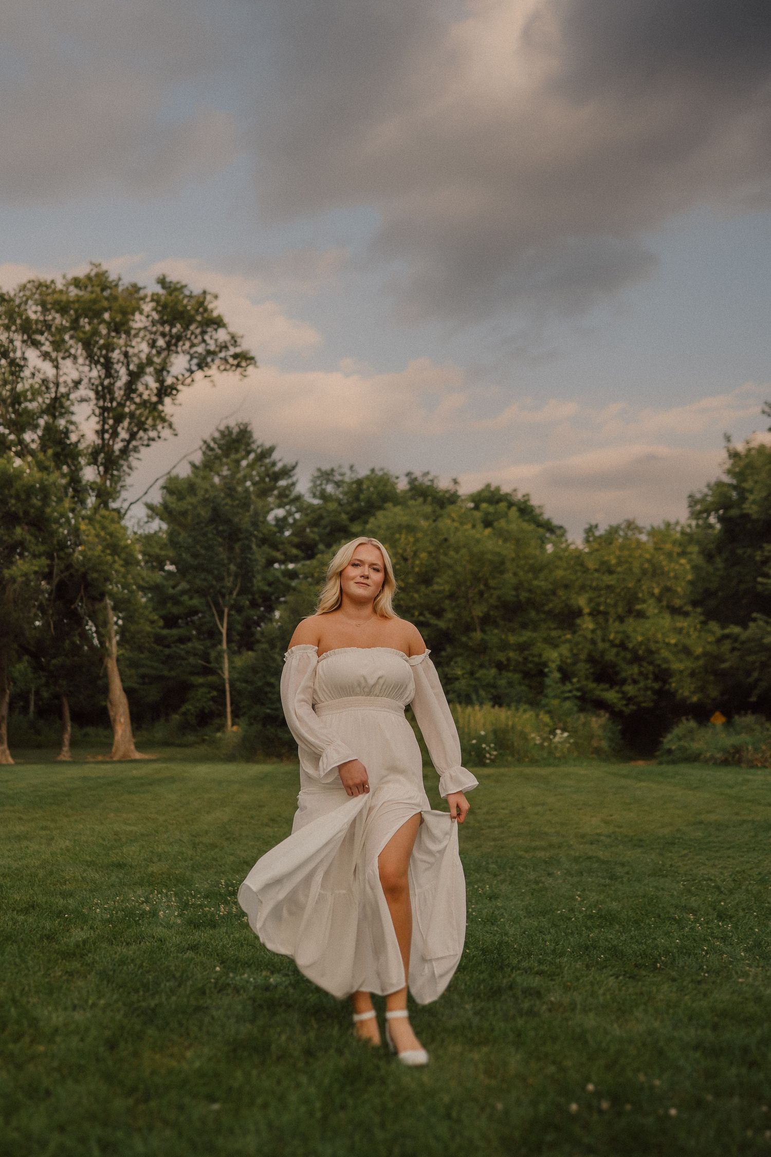 A dreamy outdoor photoshoot in a grassy field with flowing white dress movement at sunset.