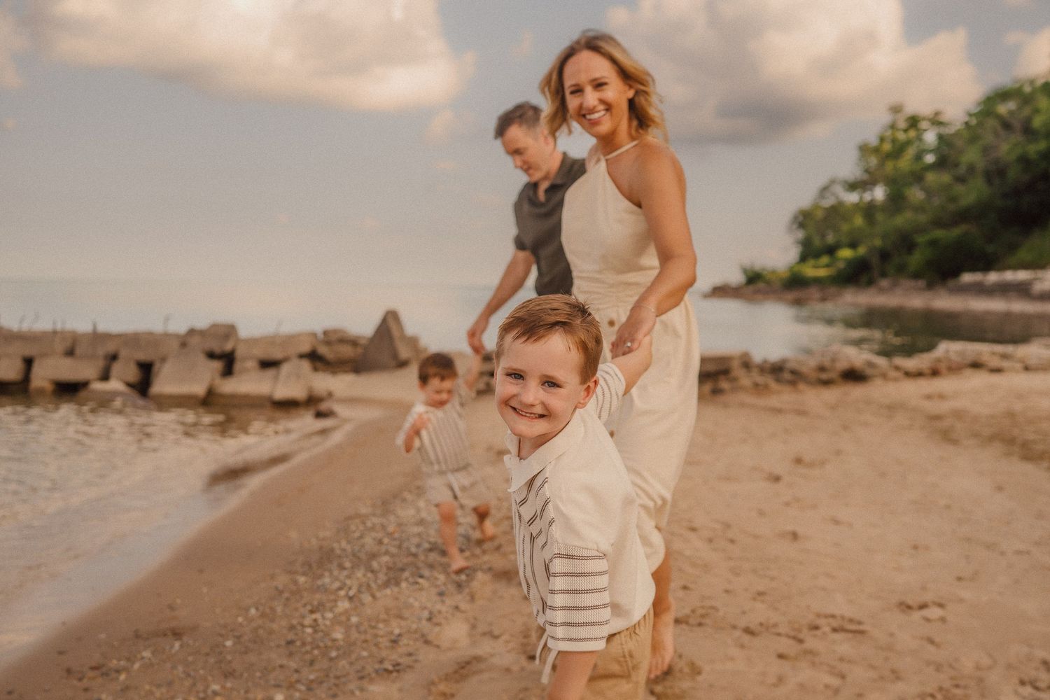 Family enjoying a sunset stroll along a scenic sandy beach with warm golden lighting.