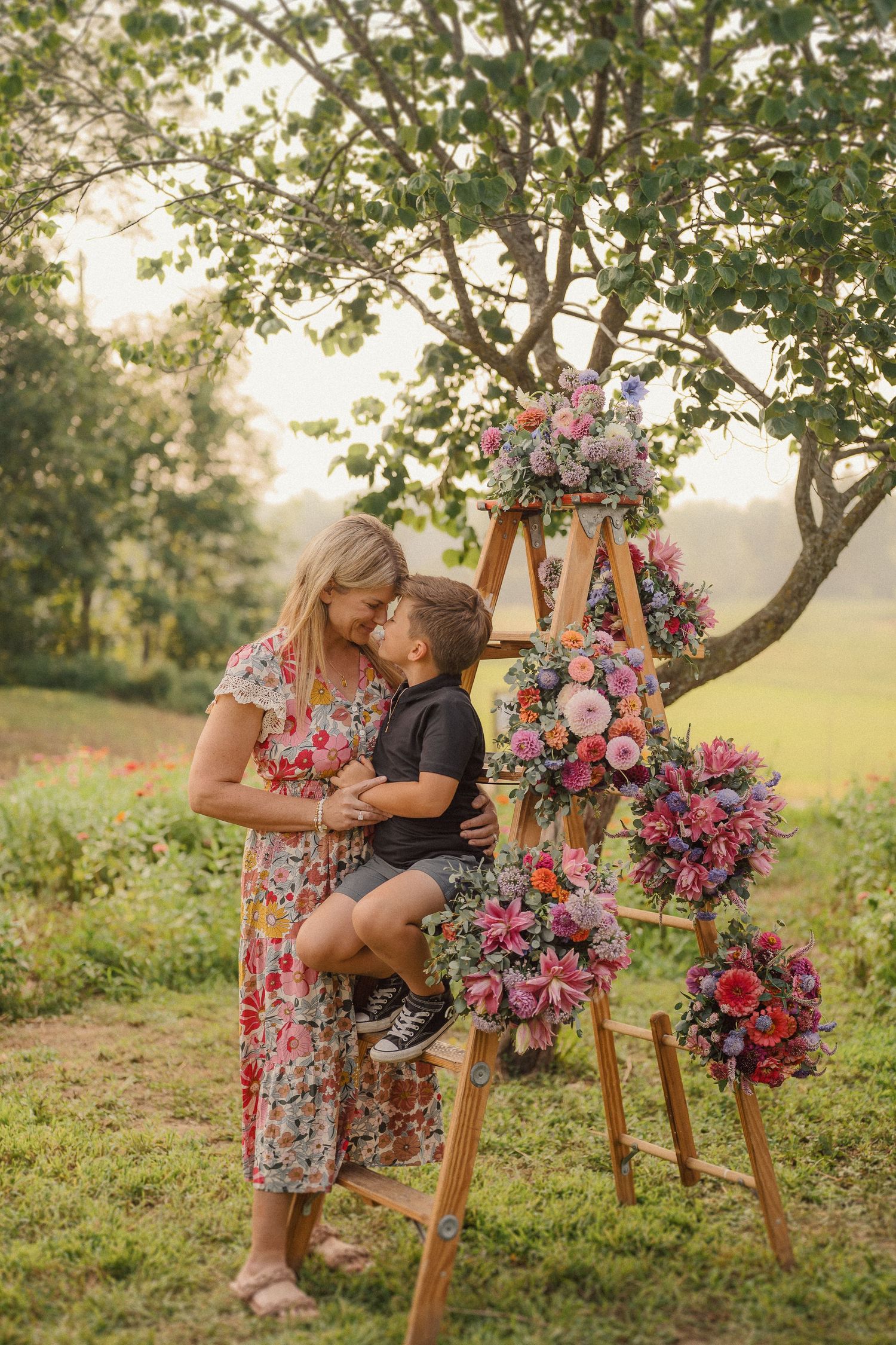 A wooden easel stands decorated with lush pink and purple flowers in a sunlit outdoor garden.