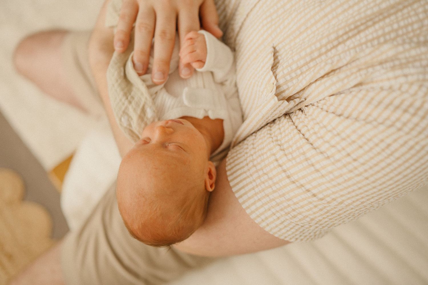 Gentle hands holding sleeping newborn wrapped in cream knit blanket.