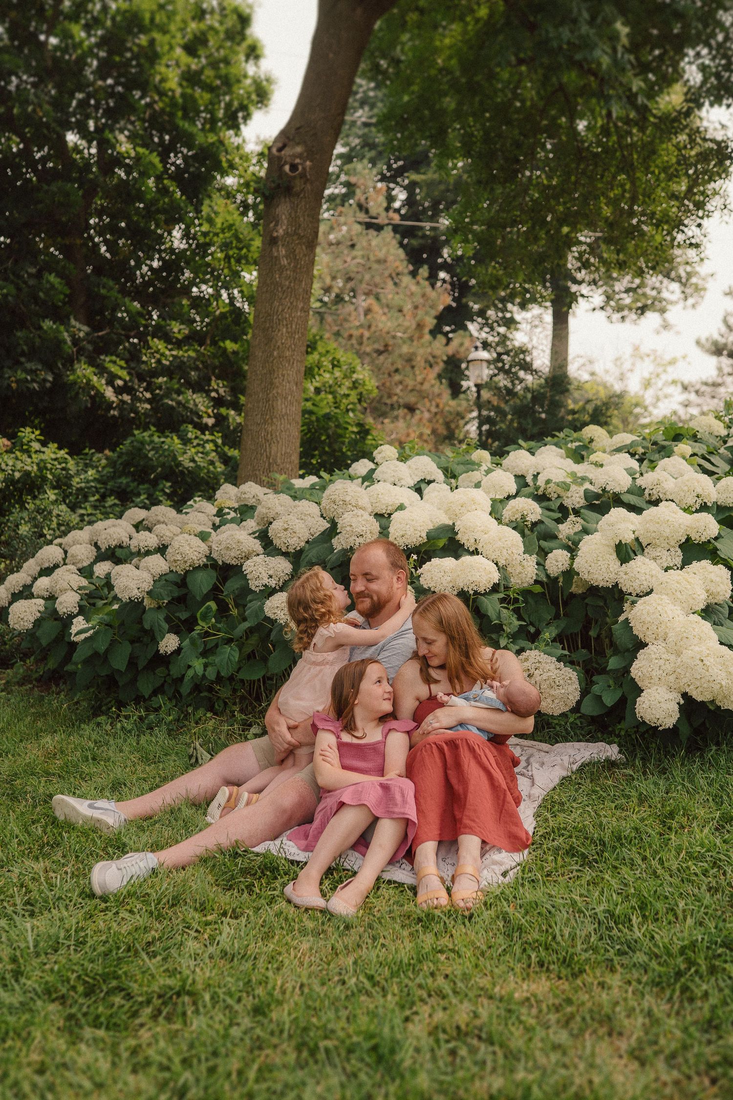 Family portrait in a garden with blooming white hydrangeas, everyone wearing coordinating pink and coral outfits.