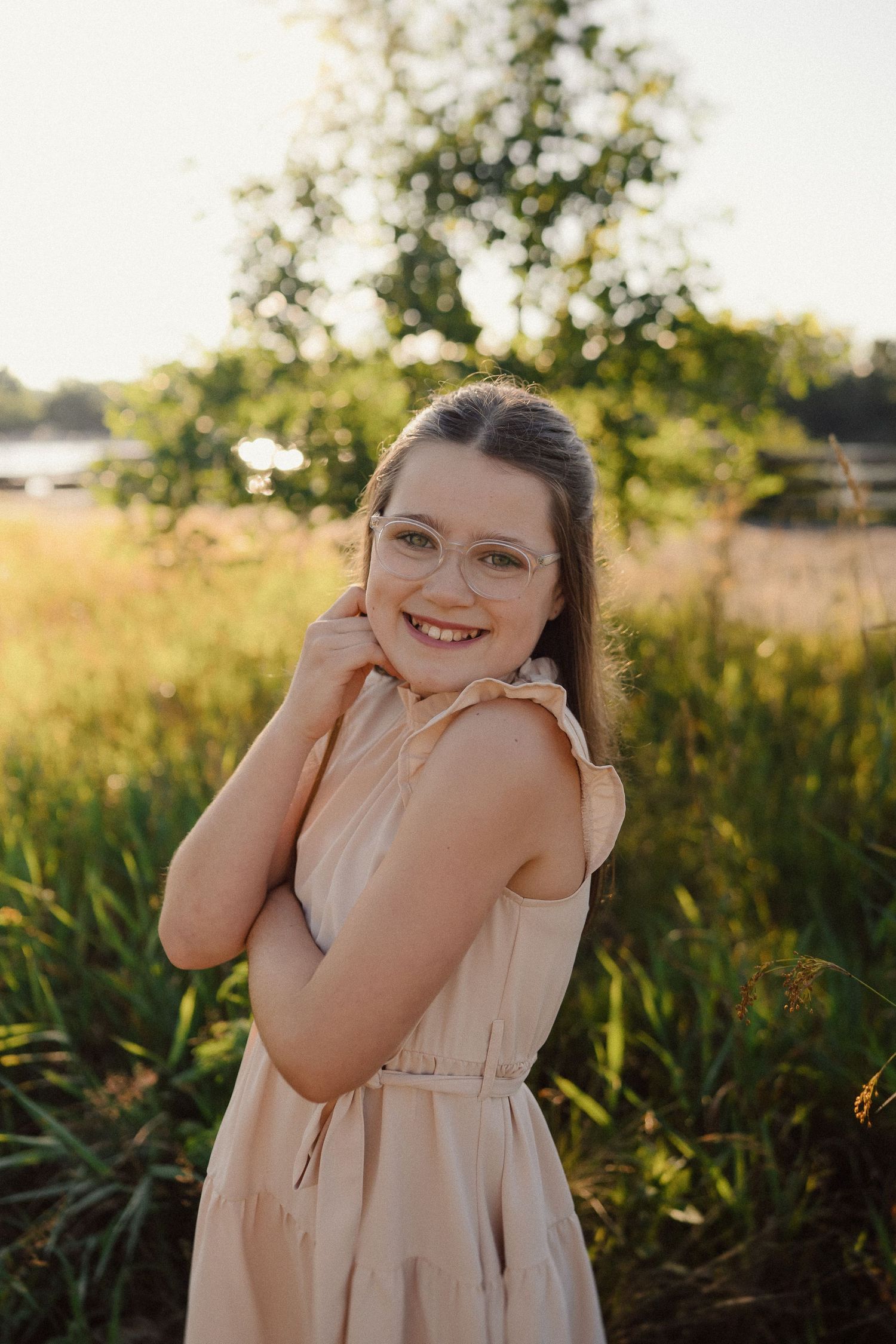 A person in a pale dress smiles joyfully while posing in a sunlit field with tall grass.