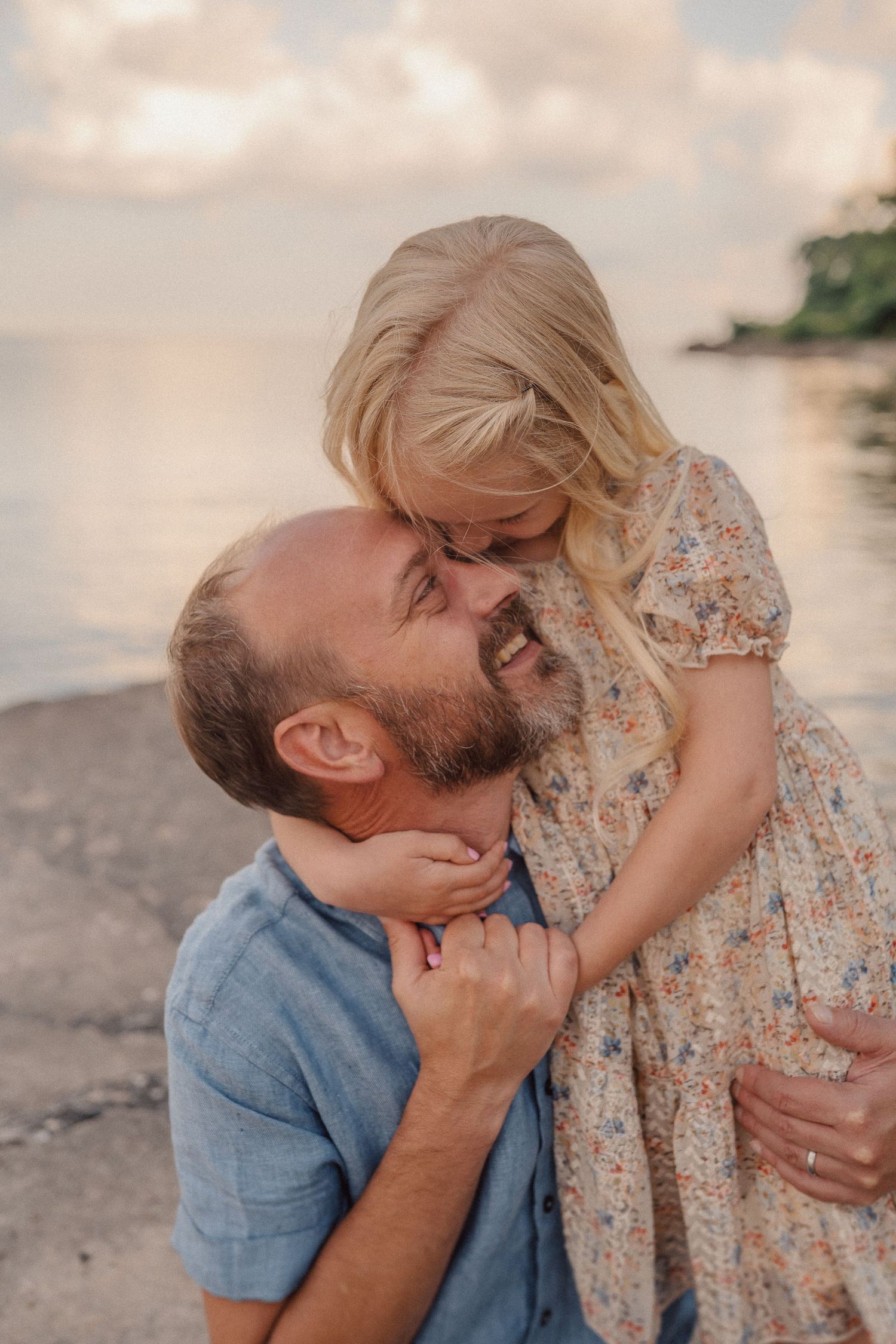 Tender moment shared between a couple embracing on a beach at sunset with soft peachy clouds in the background.