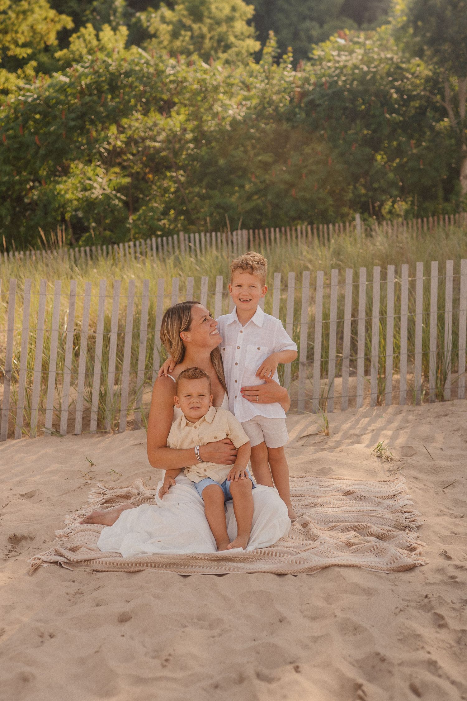 Casual beach photo session with group sitting together on sandy dunes near a wooden fence.