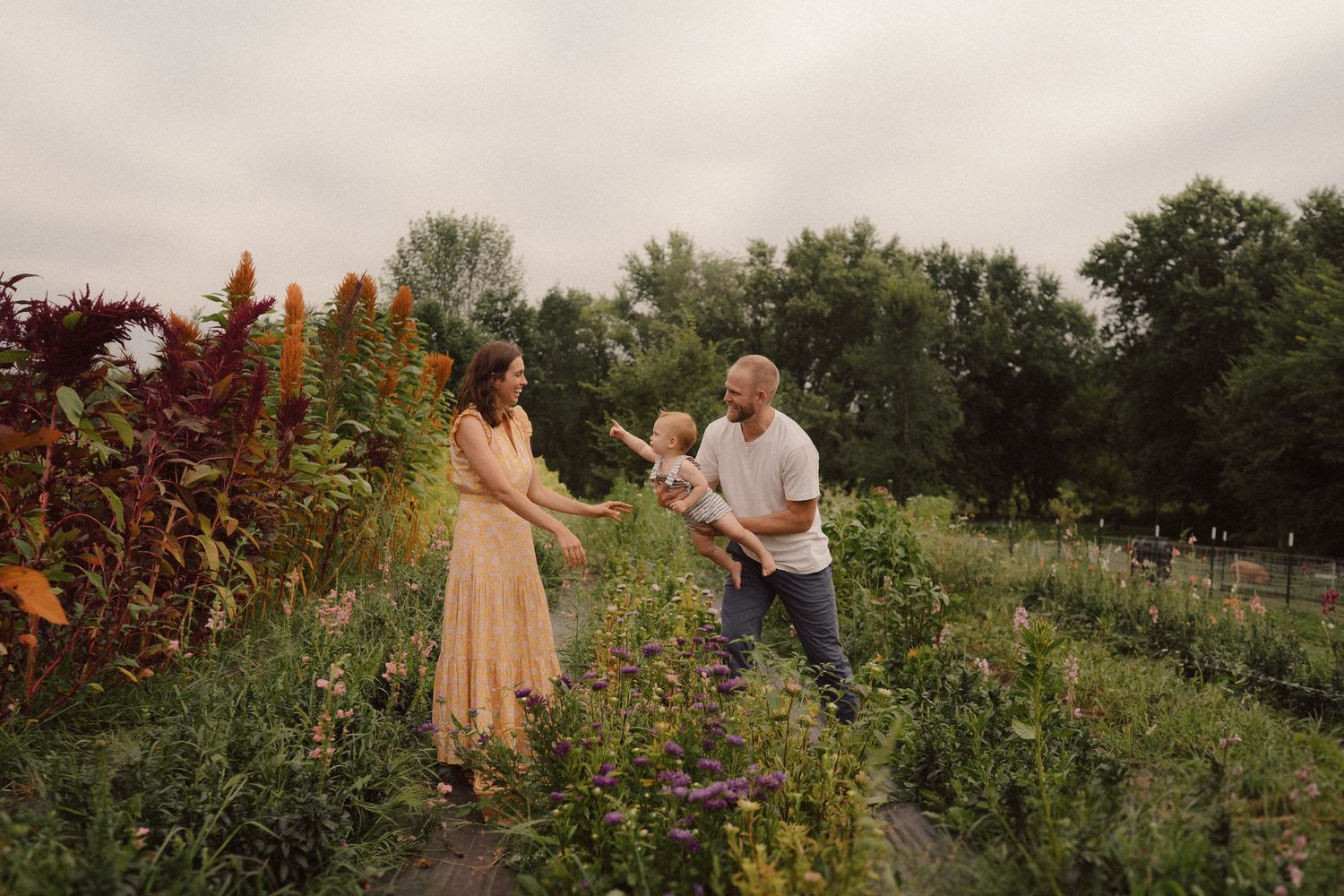 Two people standing in a blooming flower garden during golden hour as sun sets among colorful summer flowers.
