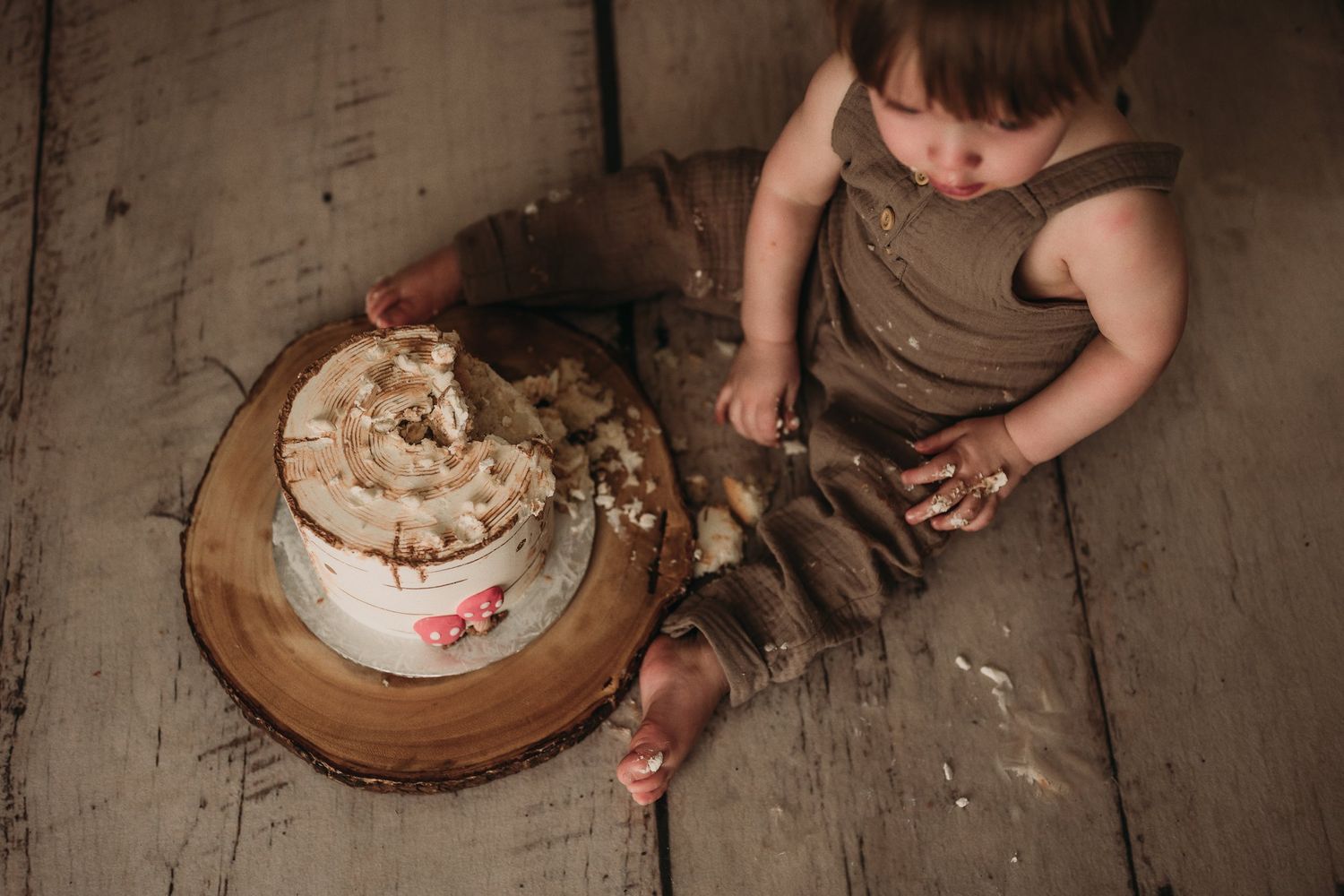 A messy cake smash scene with destroyed white frosted cake on wooden platform.
