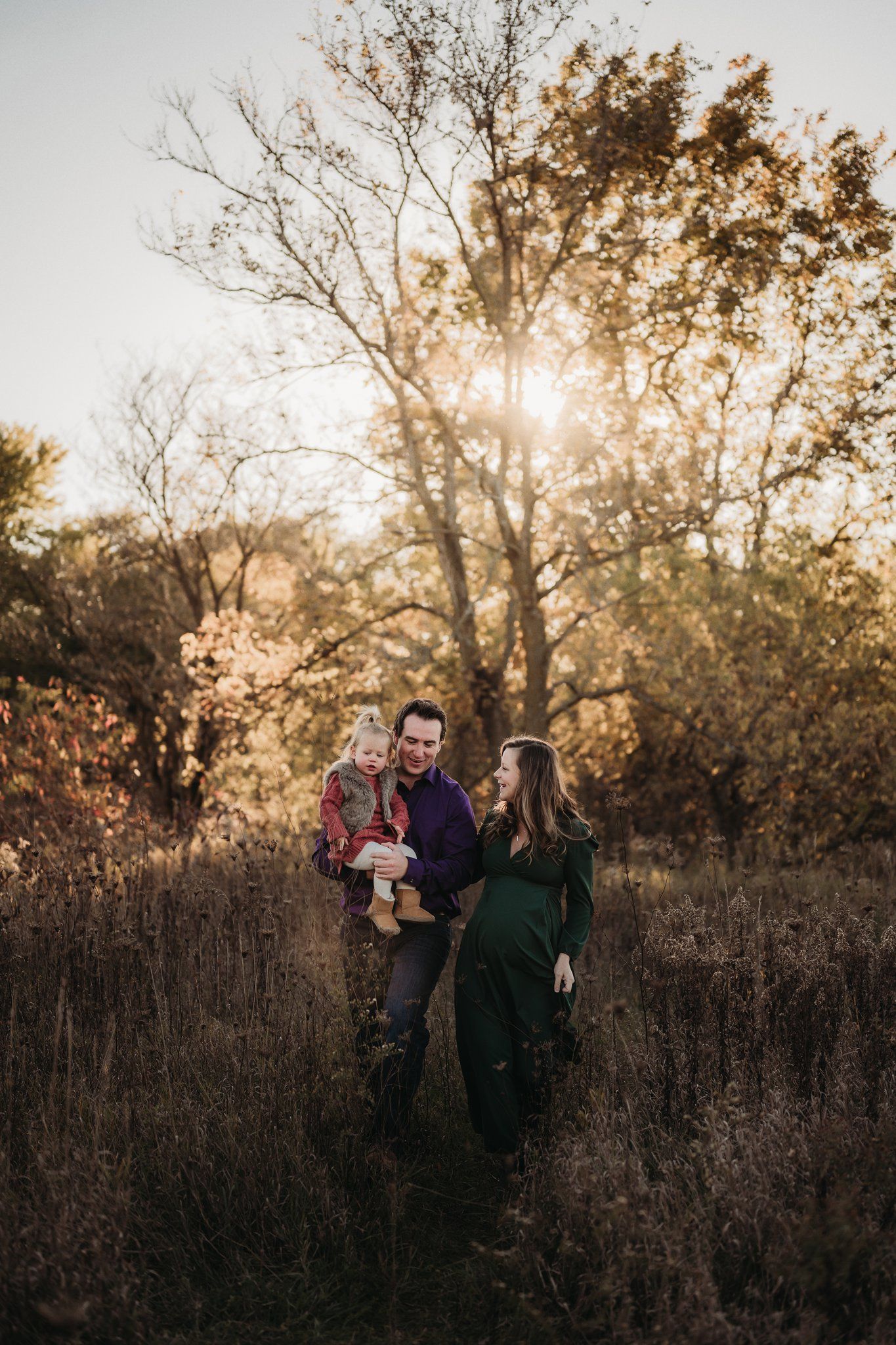 Family walking together through tall grass during golden sunset photoshoot.