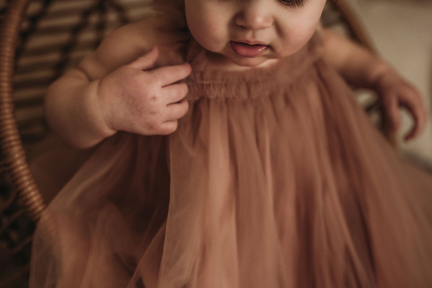 Close-up detail of dusty rose tulle dress fabric and tiny hands.