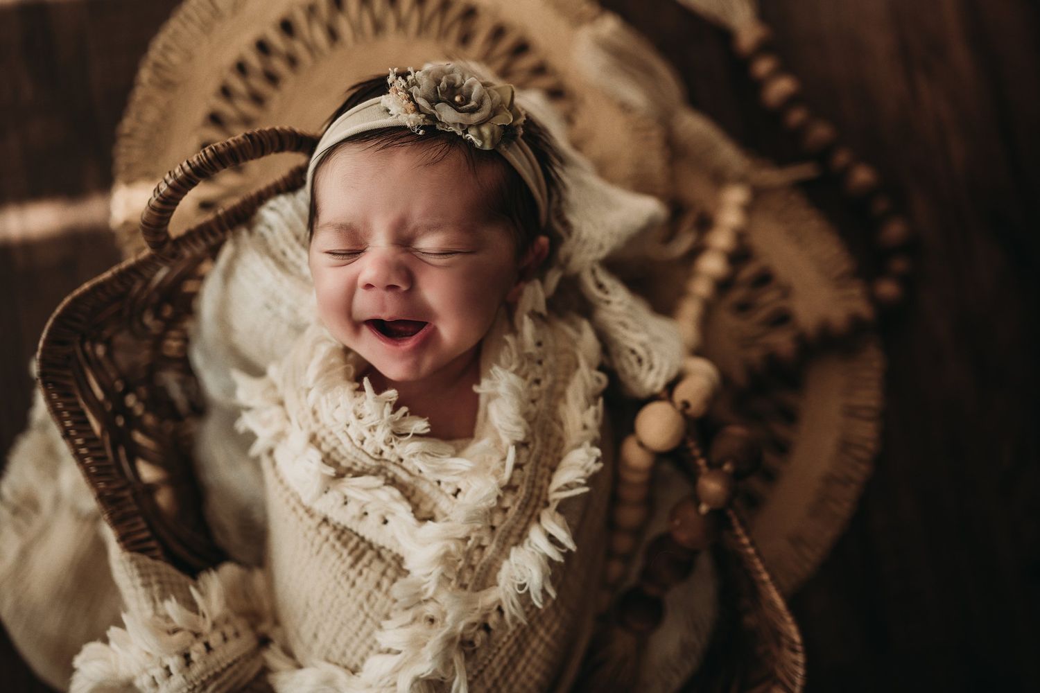 Laughing baby in cream knit wrap and vintage headpiece in wicker bassinet.