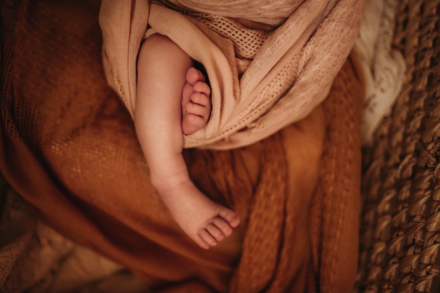 Close-up of tiny baby feet peeking out from a brown swaddle blanket.