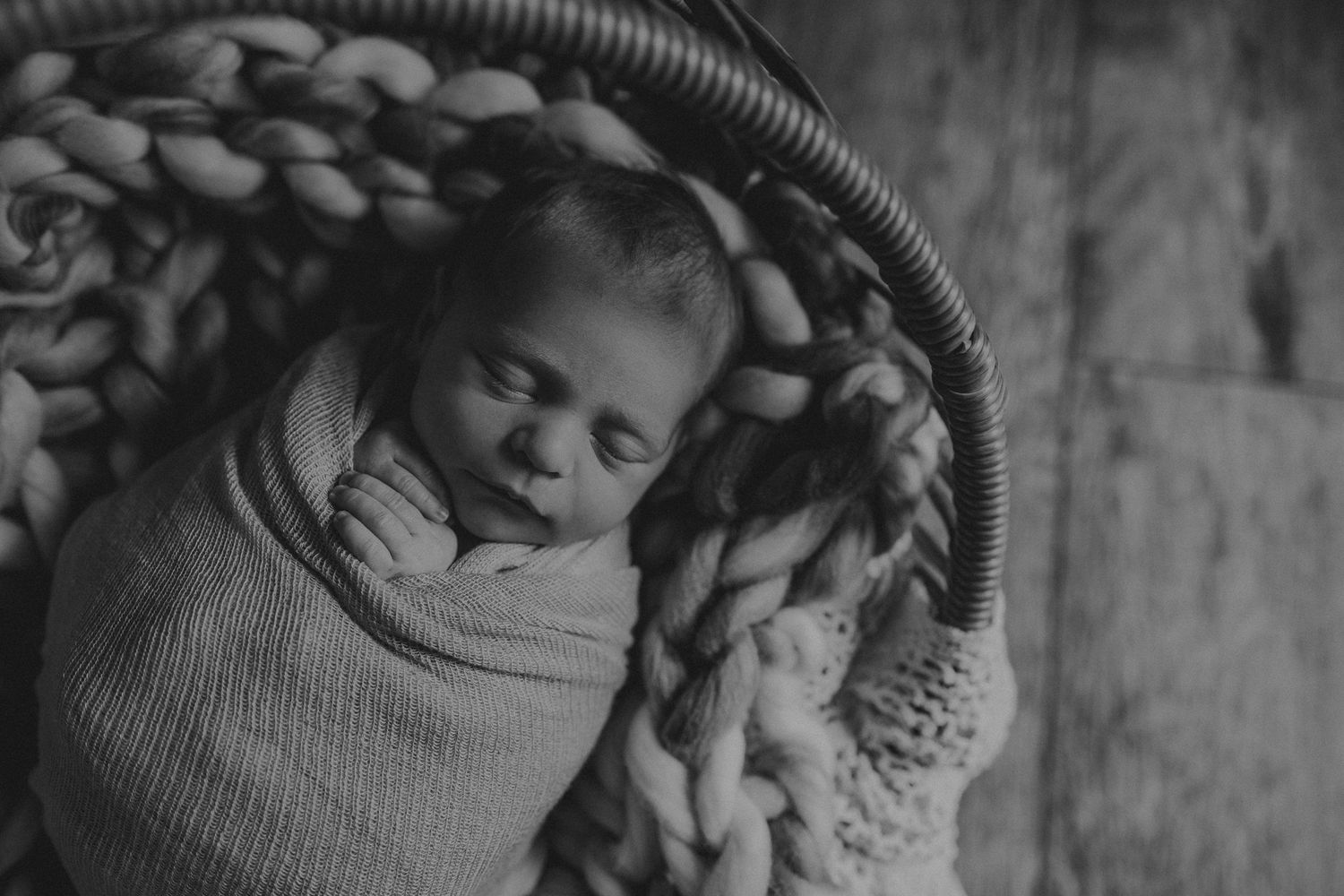 Black and white portrait of sleeping baby wrapped in knitted blanket in basket.