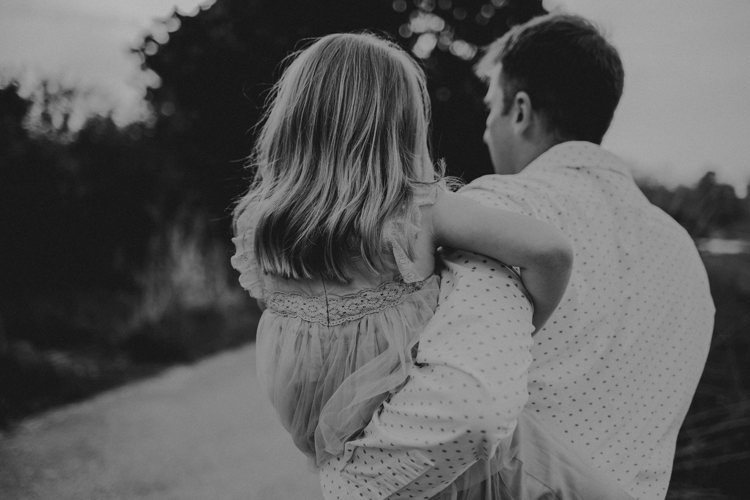 A tender black and white moment captured from behind on a quiet path at dusk.