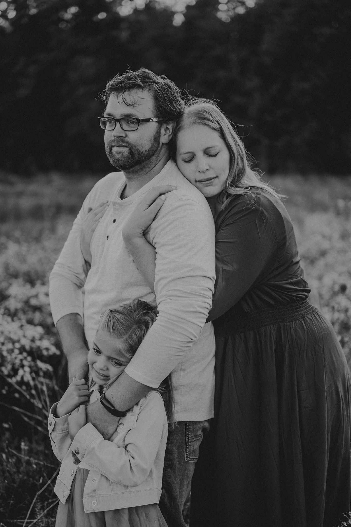 Black and white family portrait showing tender embrace in natural setting.