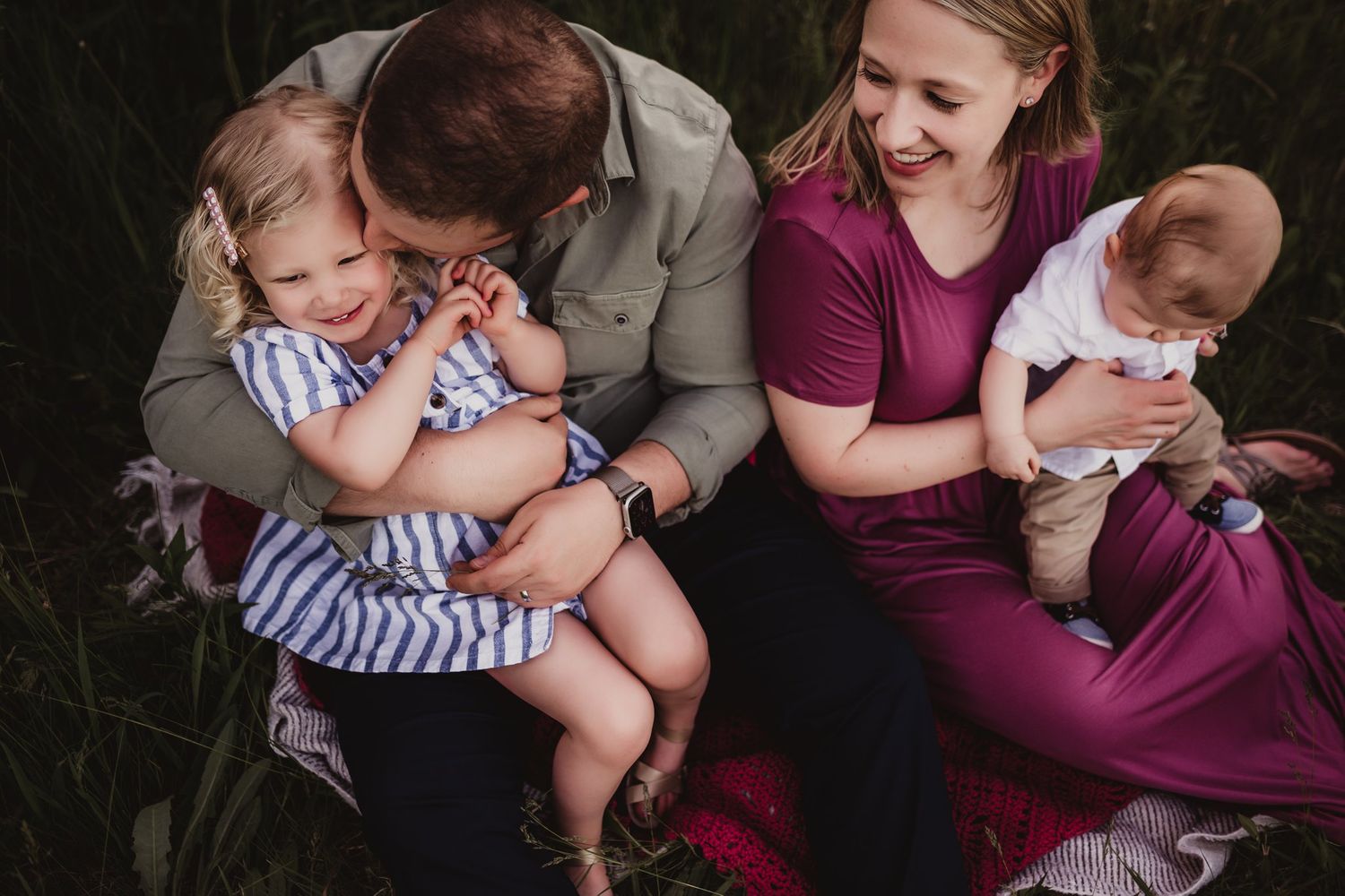 An intimate family portrait showing tender moments between parents and children outdoors.