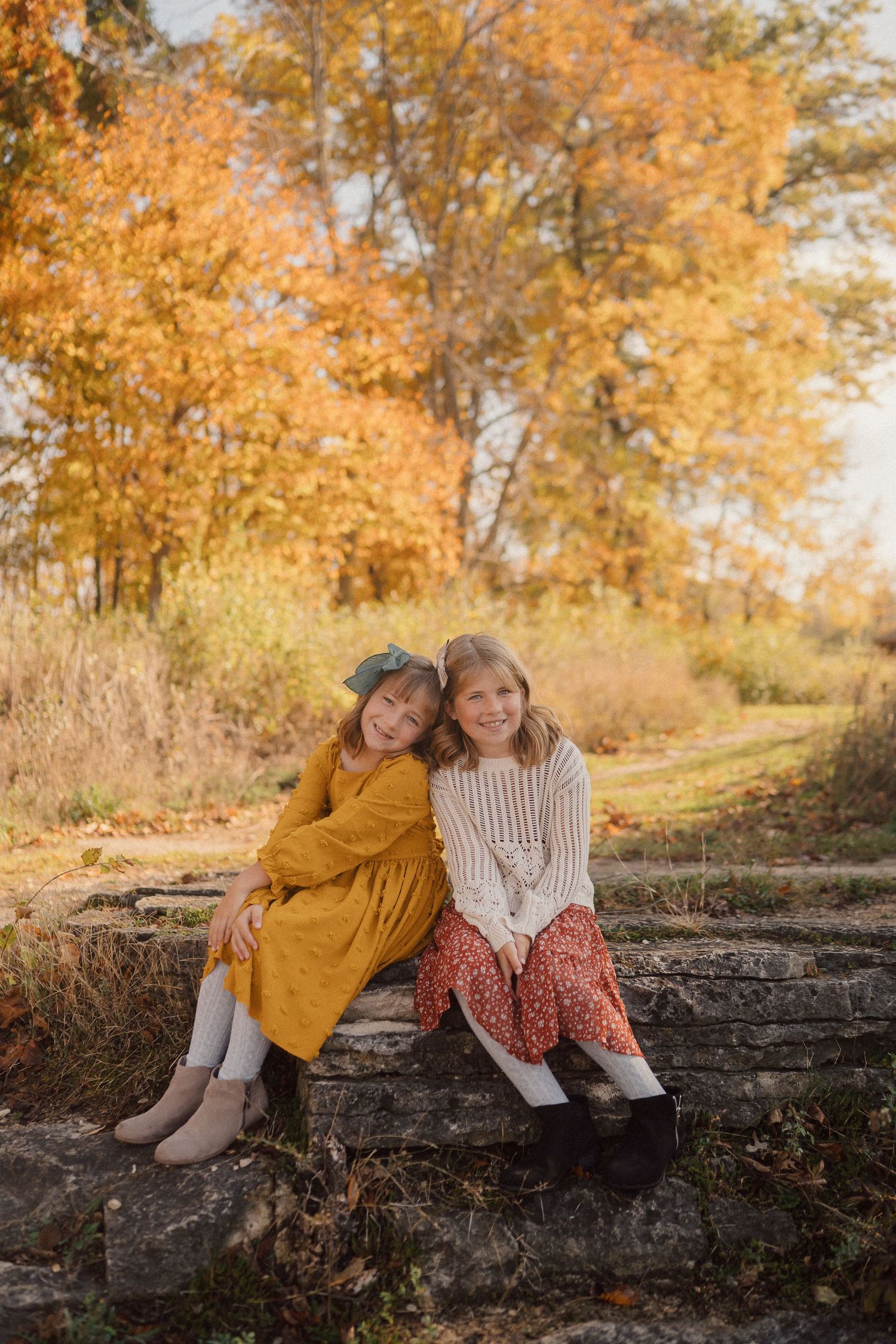 Three people relaxing on a stone wall against a backdrop of autumn trees with golden leaves.