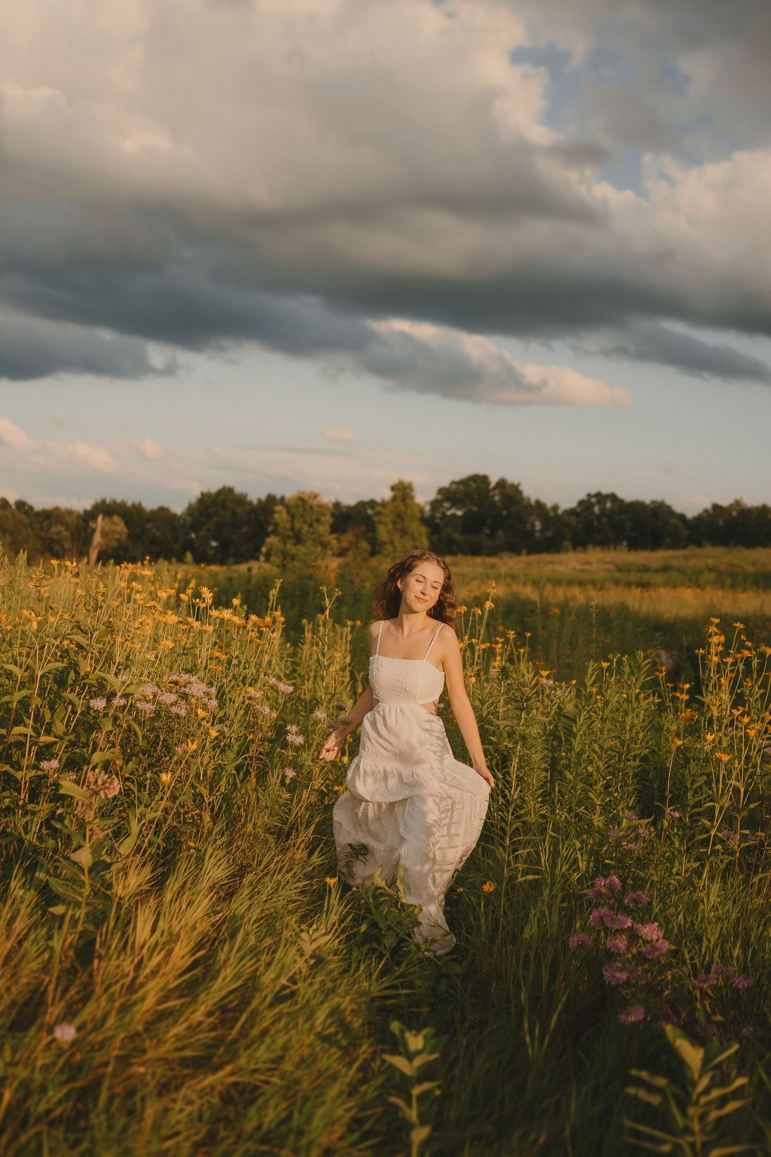 Dreamy summer portrait in a meadow with dramatic storm clouds and golden light.