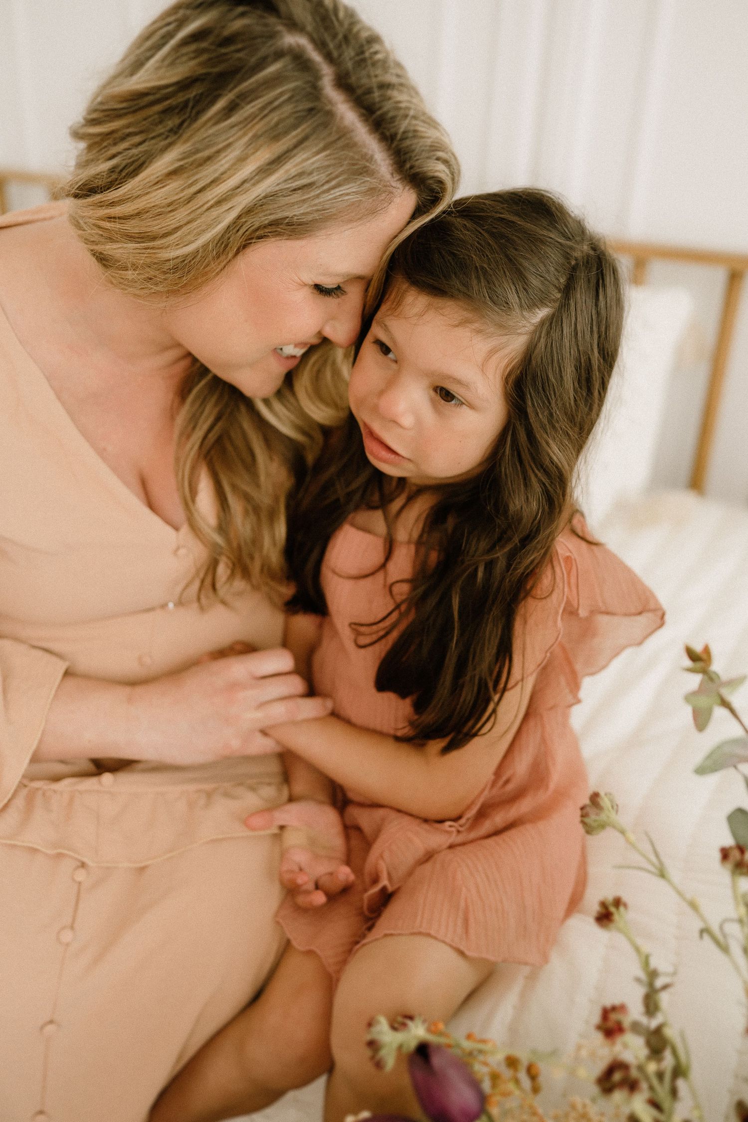 A tender moment shared between a parent and child wearing matching pink dresses while sitting together on a bed.