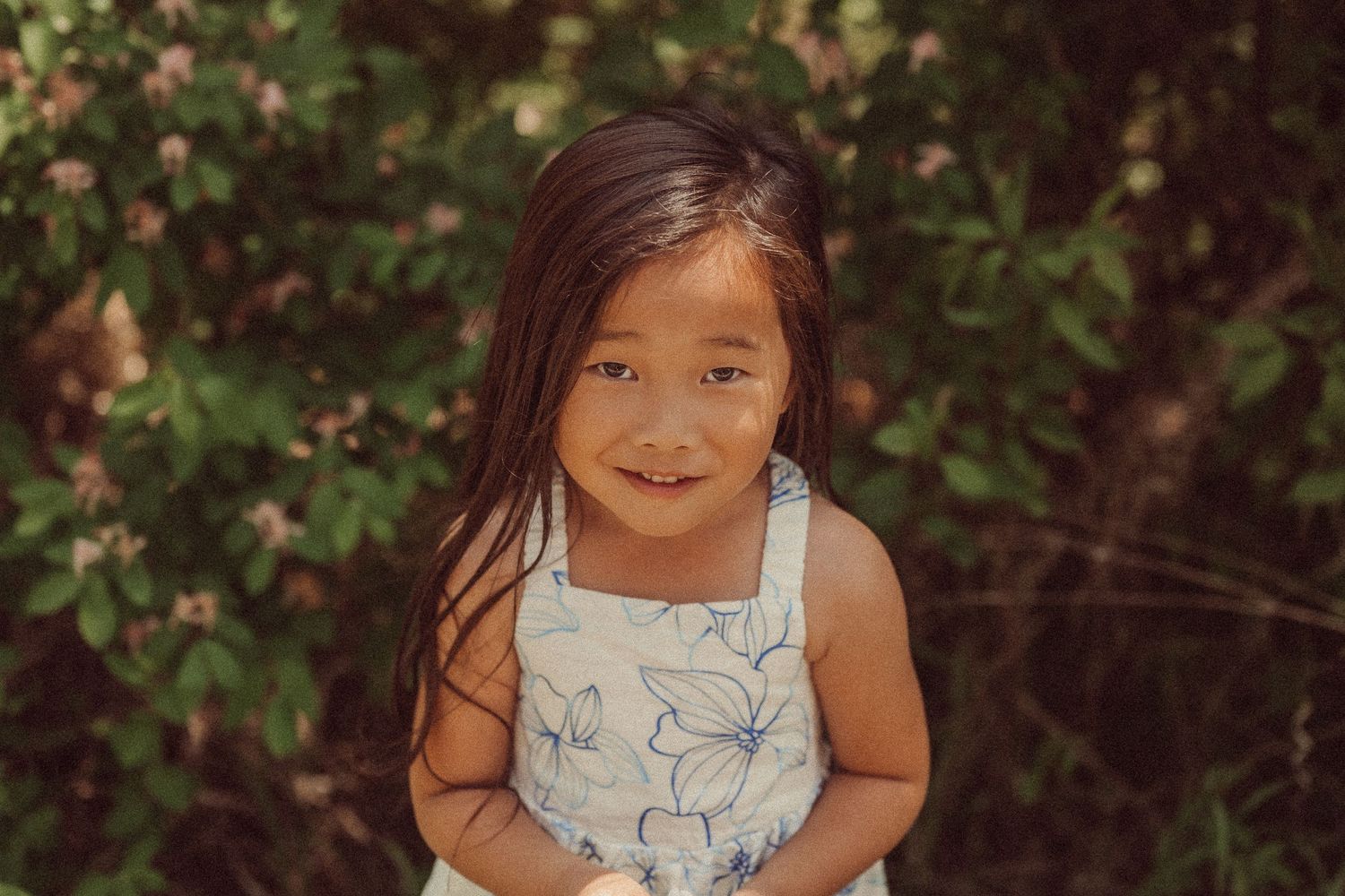 A summer portrait in a floral dress against a backdrop of green foliage.